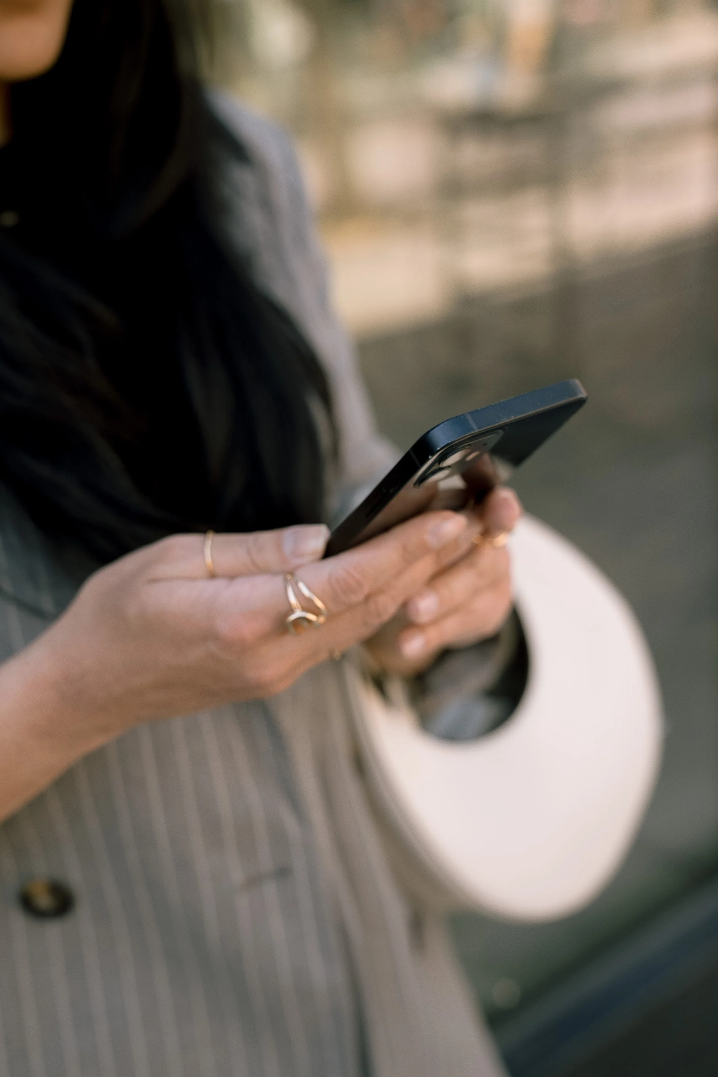 A woman holding a smartphone, with a roll of paper towels in her other hand, wearing rings and a striped blazer.