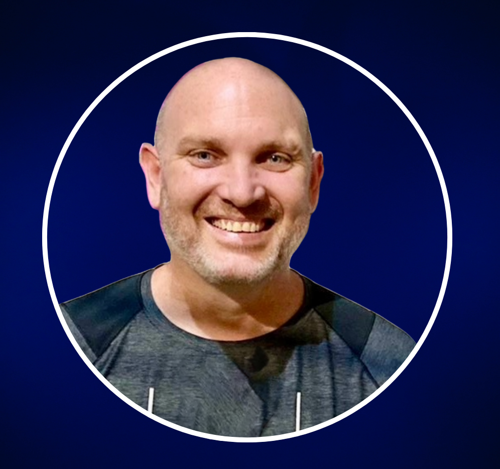 A smiling man with a beard and wearing a sports shirt against a gray background.