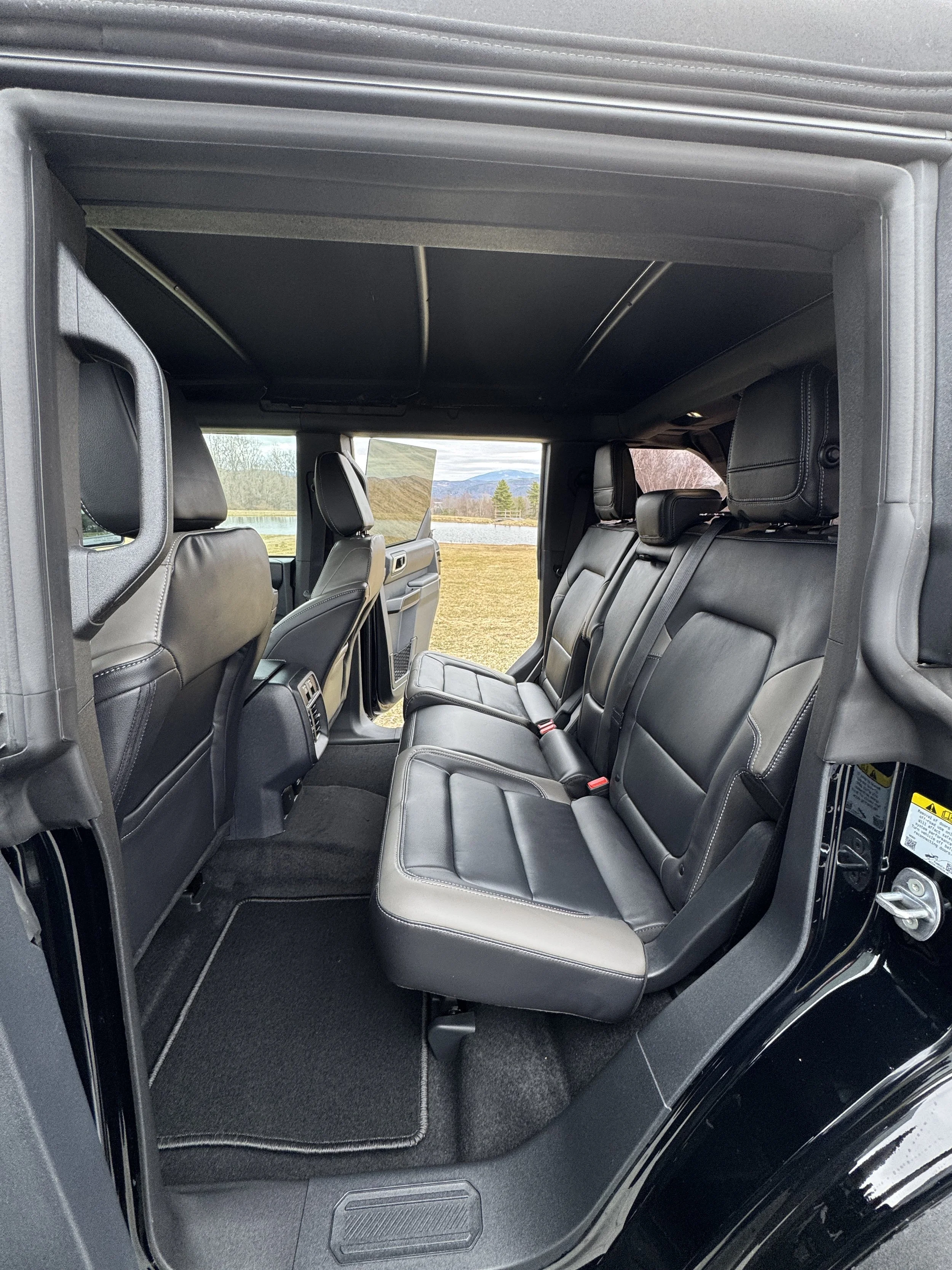 Interior of Vermont Wayfinders Bronco with black leather seats, showing a view of the rear seating area and open car door.