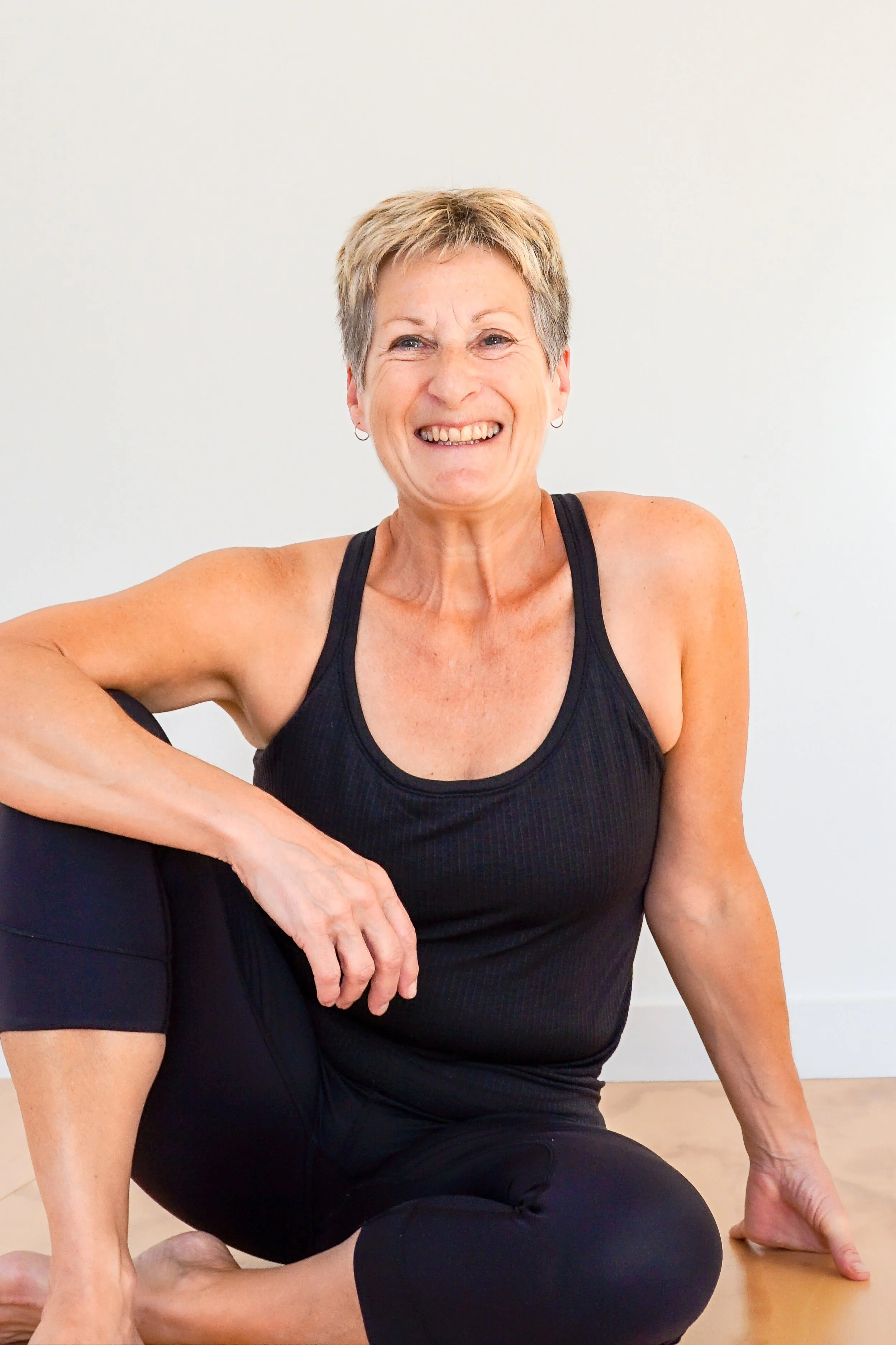 Older woman in black workout attire sitting cross-legged and smiling.