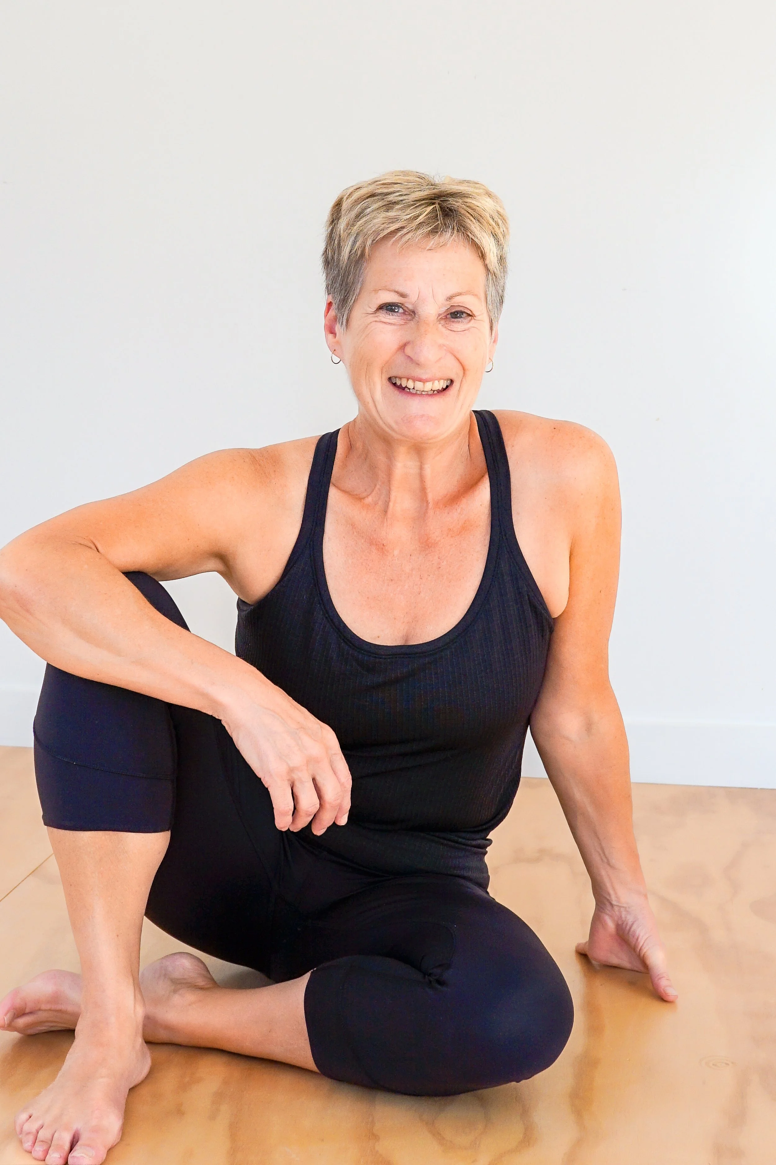 Smiling woman in athletic wear sitting on the floor in a yoga pose.