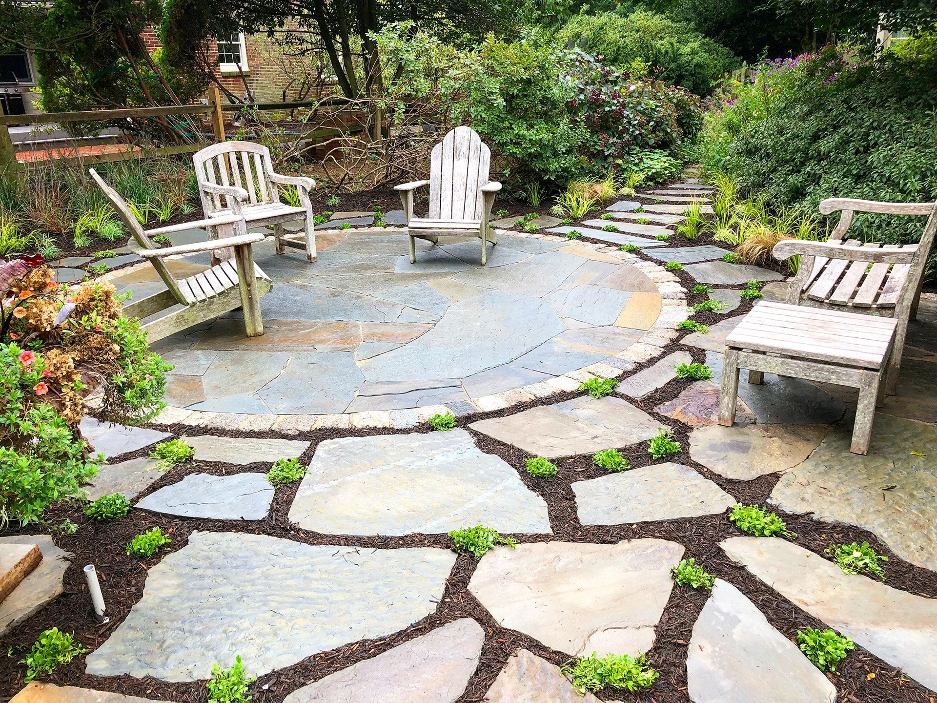 Garden patio with Adirondack chairs, stone pavers, and surrounding greenery