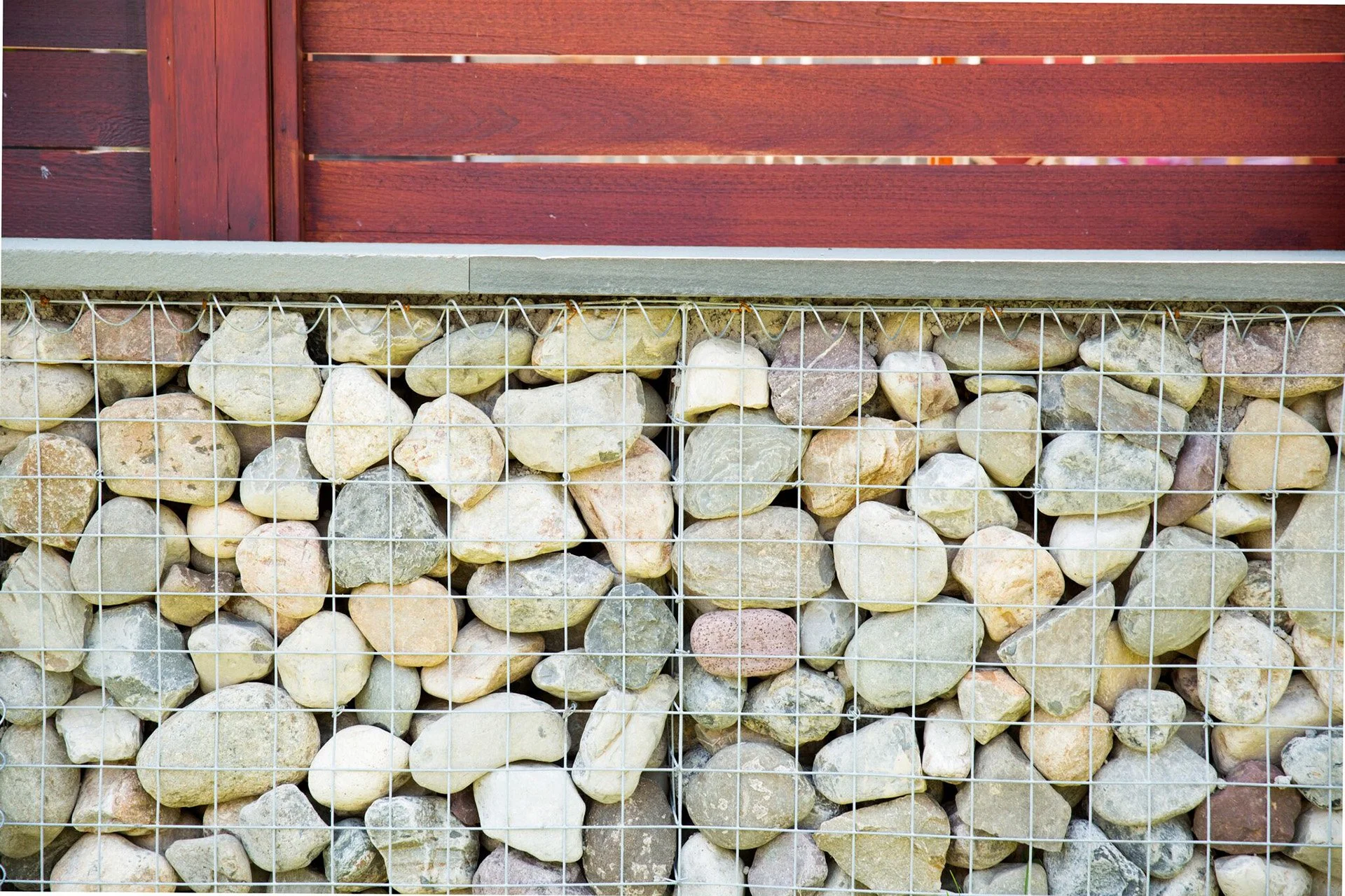 Gabion wall with stones behind wire mesh, topped with wooden fence.
