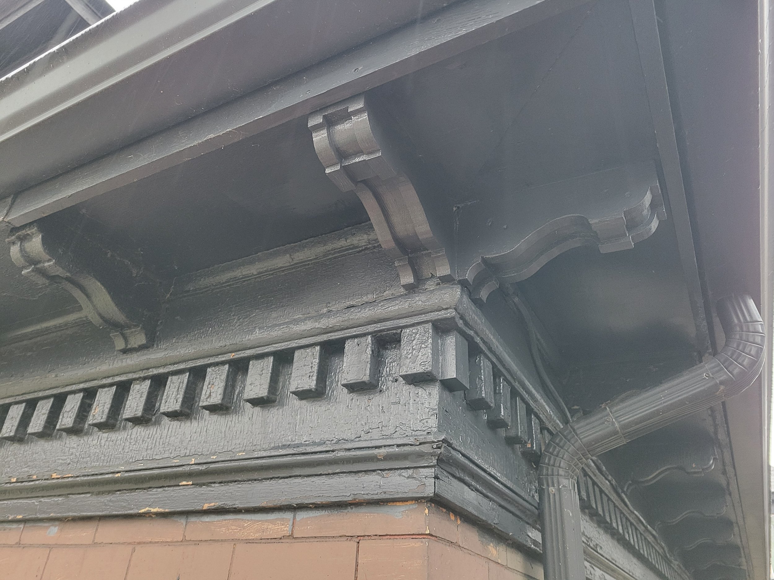 Close-up of the underside of a black-painted wooden porch roof with decorative trim and rain gutter.