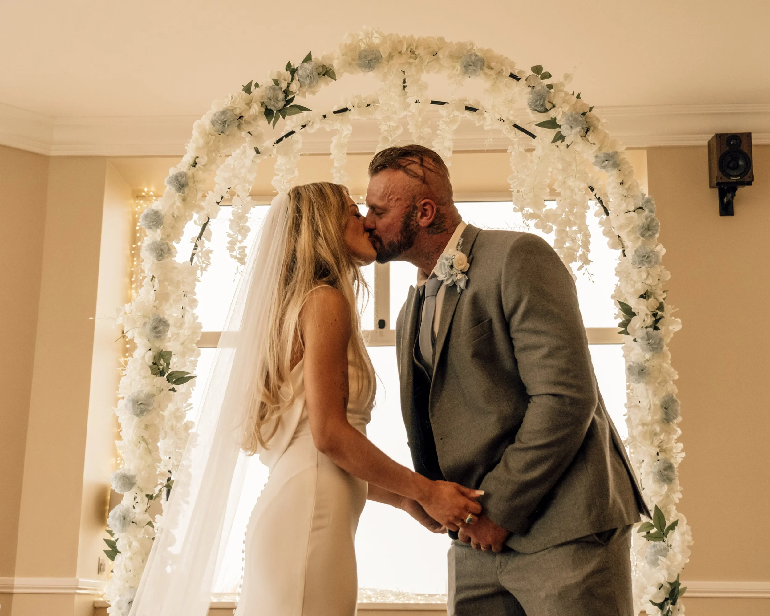 A bride and groom kissing under a floral wedding arch.