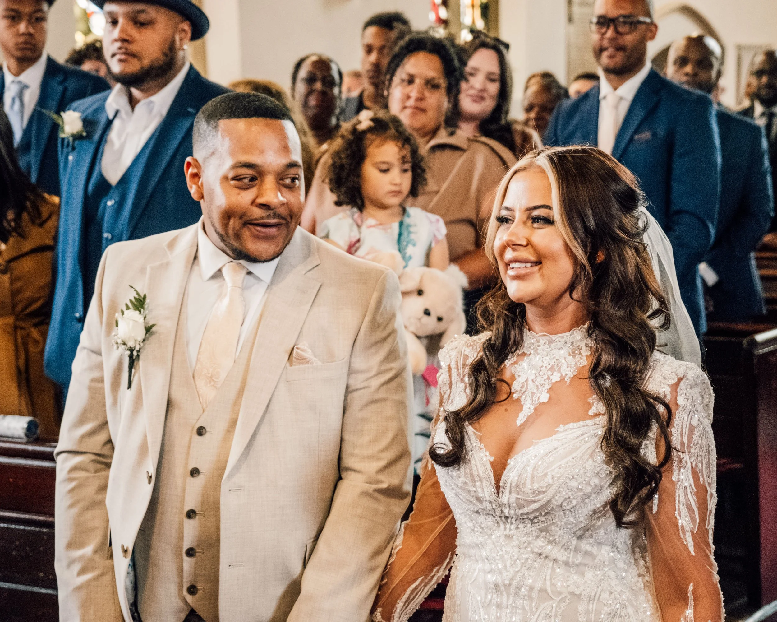 A group of wedding guests, including a bride and groom, gathered inside a church, dressed in formal attire, during a wedding ceremony.