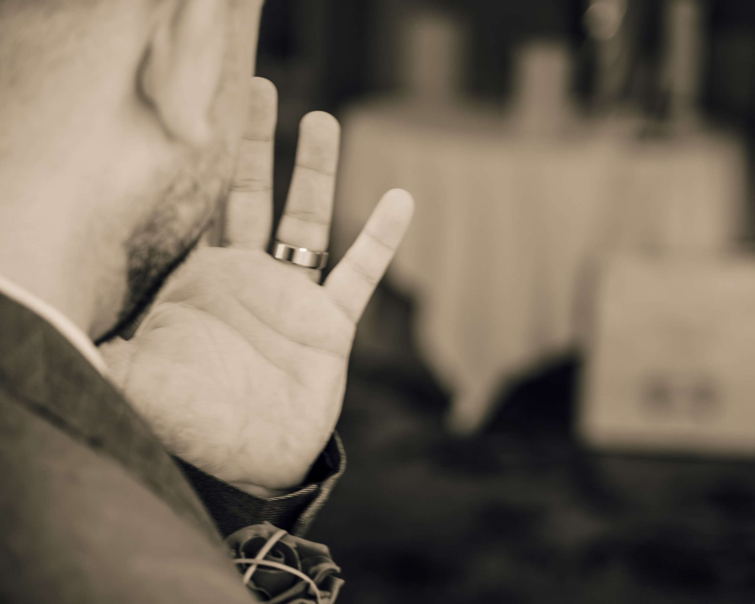Close-up of a person's hand wearing a ring, with a blurred background and a pair of sneakers visible at the bottom.