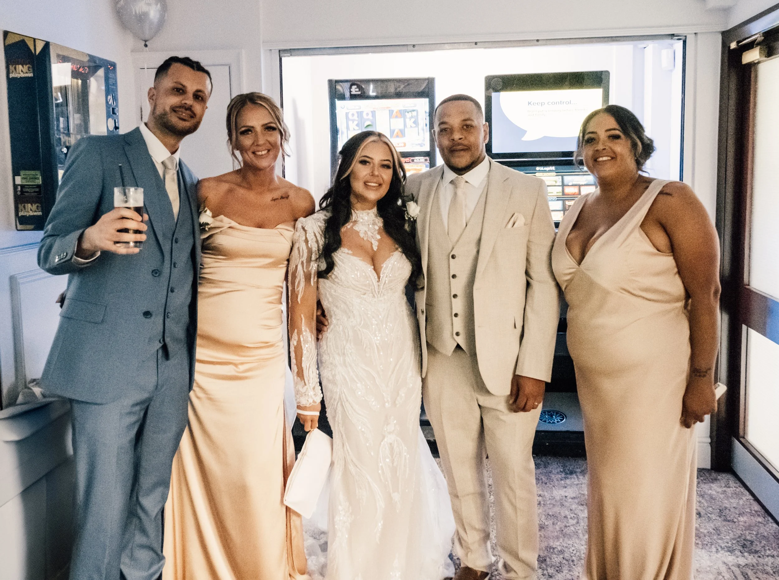 Group of six people dressed in wedding attire standing together indoors, smiling for a photo.