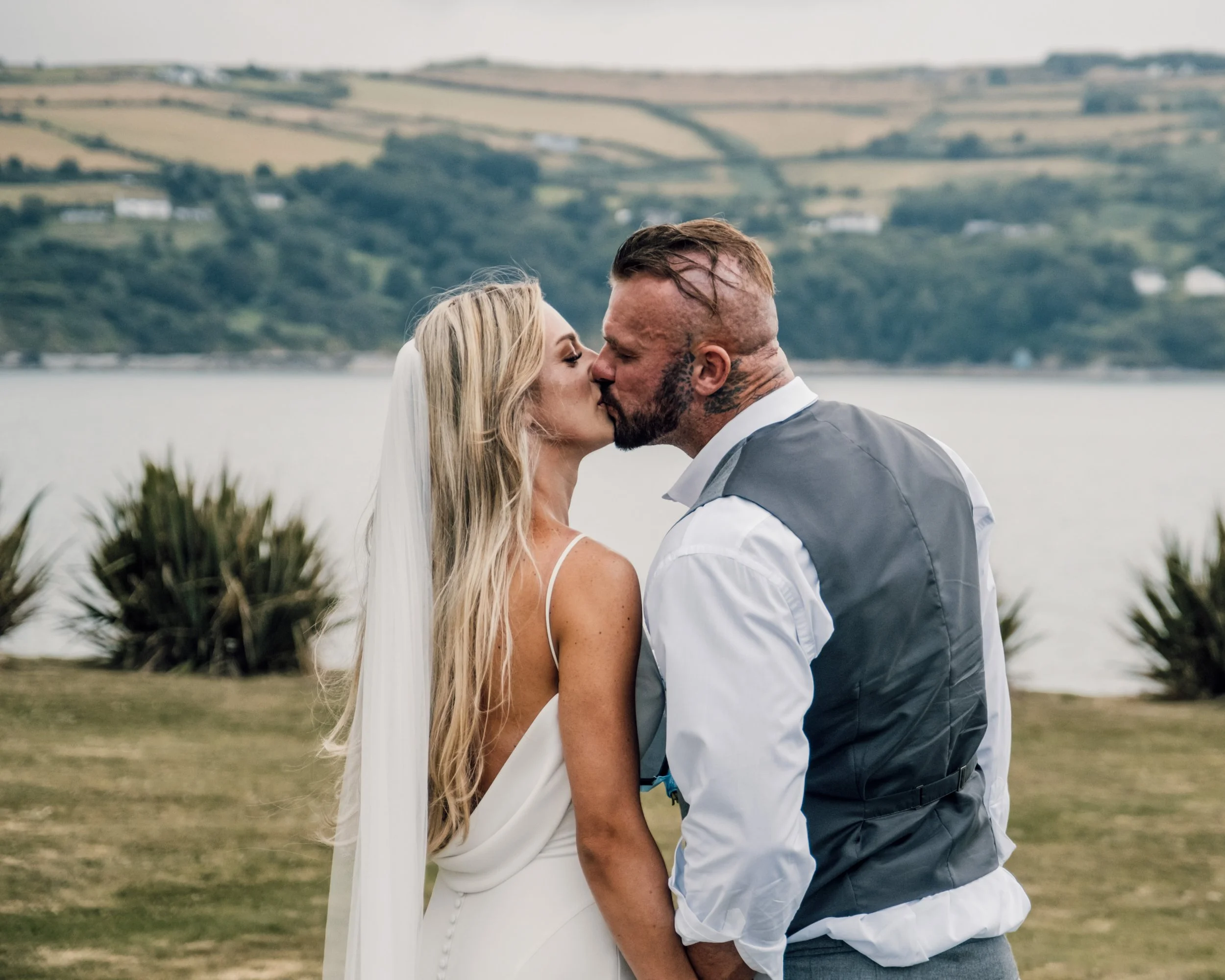 A couple sharing a kiss outdoors near water with hills in the background