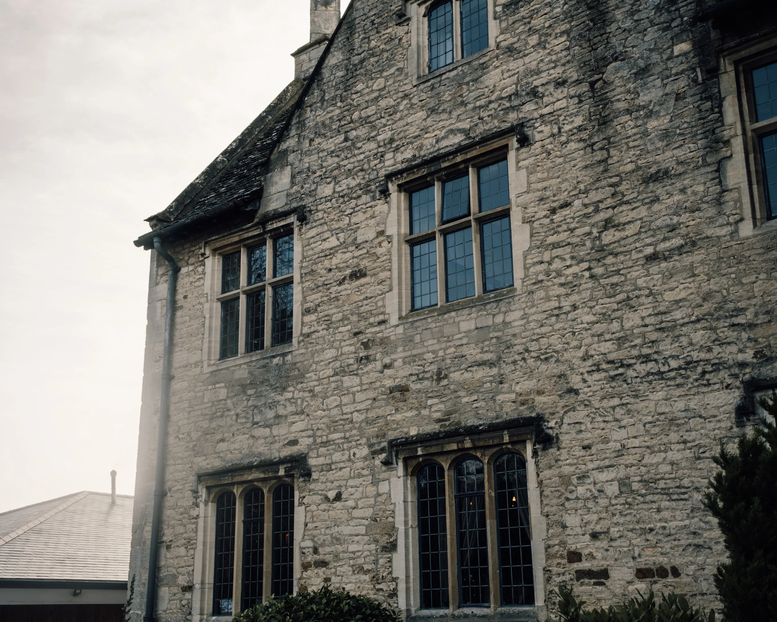 Stone building with multiple blue-tinted windows and a dark roof, with a chimney in the background.