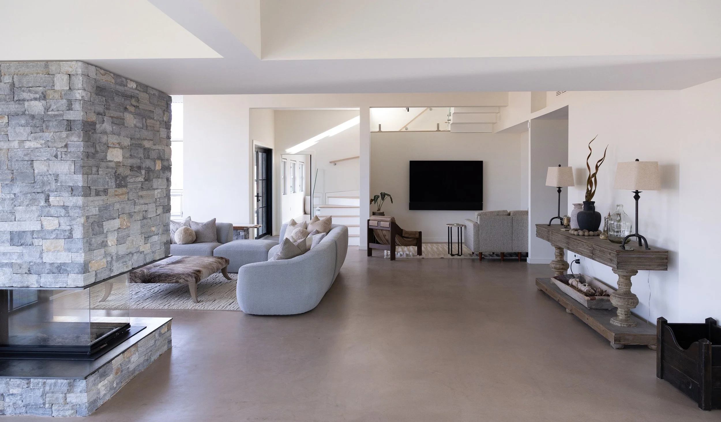 Open living room with modern furniture, stone fireplace, wall-mounted TV, and decorative elements.