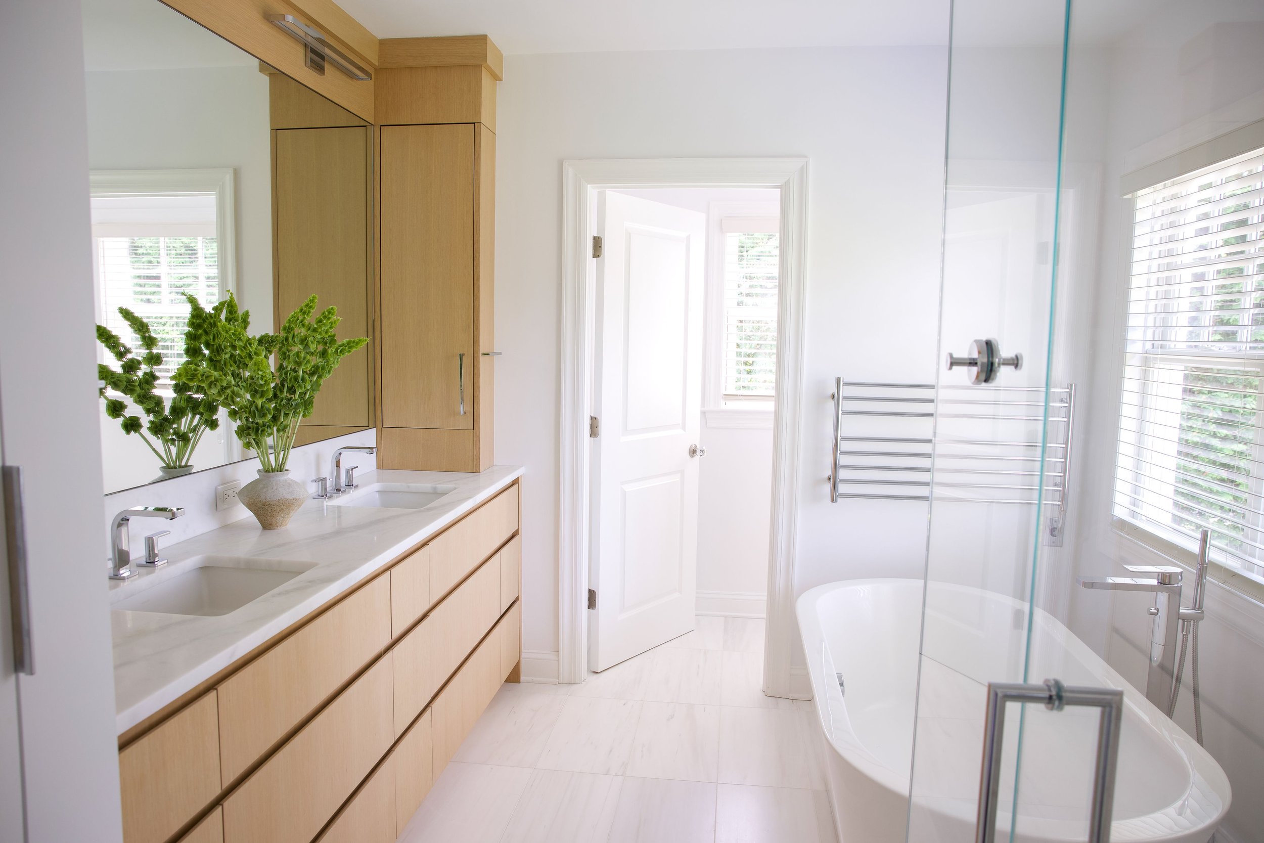 Bright bathroom with dual sinks, wooden cabinetry, a bathtub, towel rack, and window blinds.