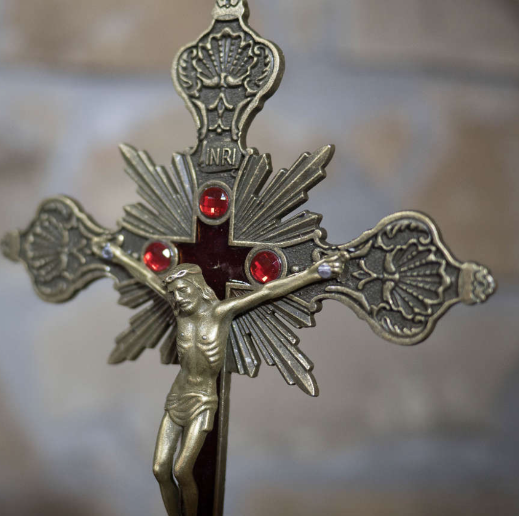 A religious pendant featuring a crucifix of Jesus Christ, with decorative elements and red gemstones.