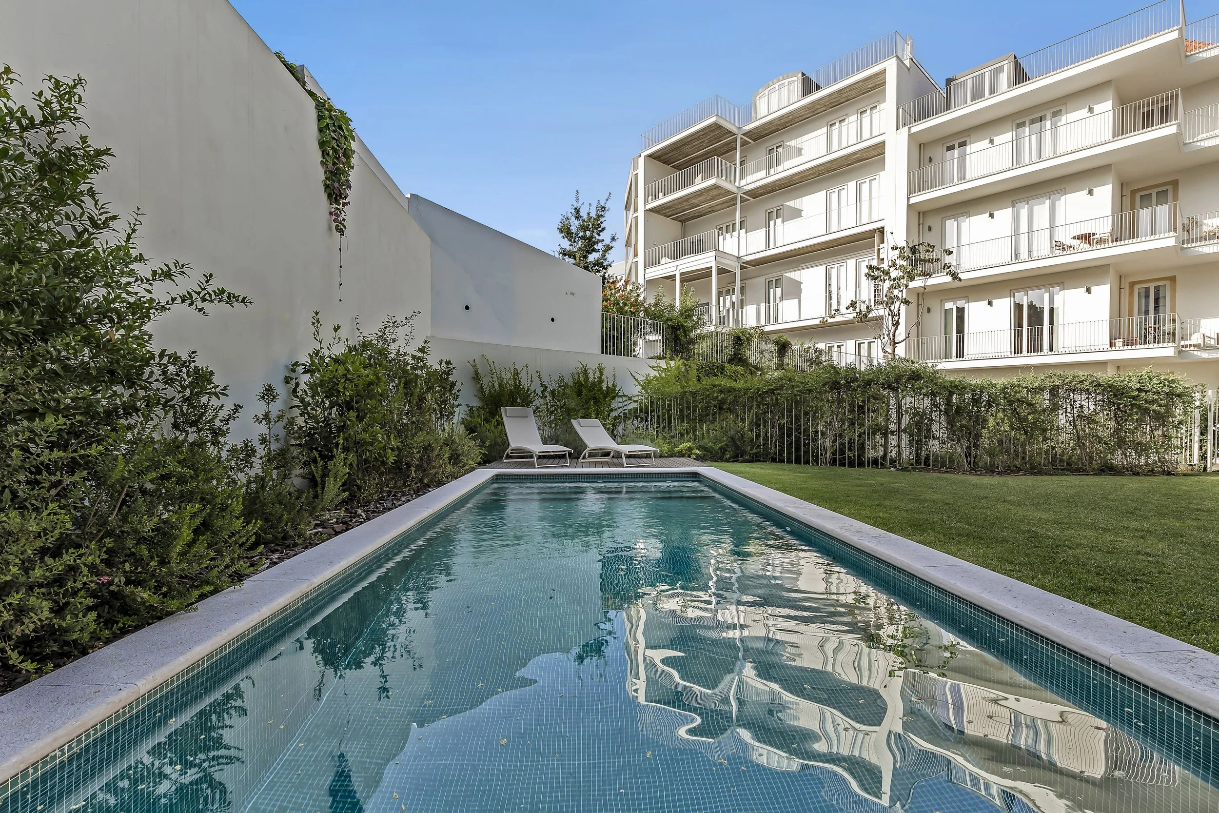 Piscina no jardim do condomínio com cadeiras de descanso e apartamento moderno ao fundo