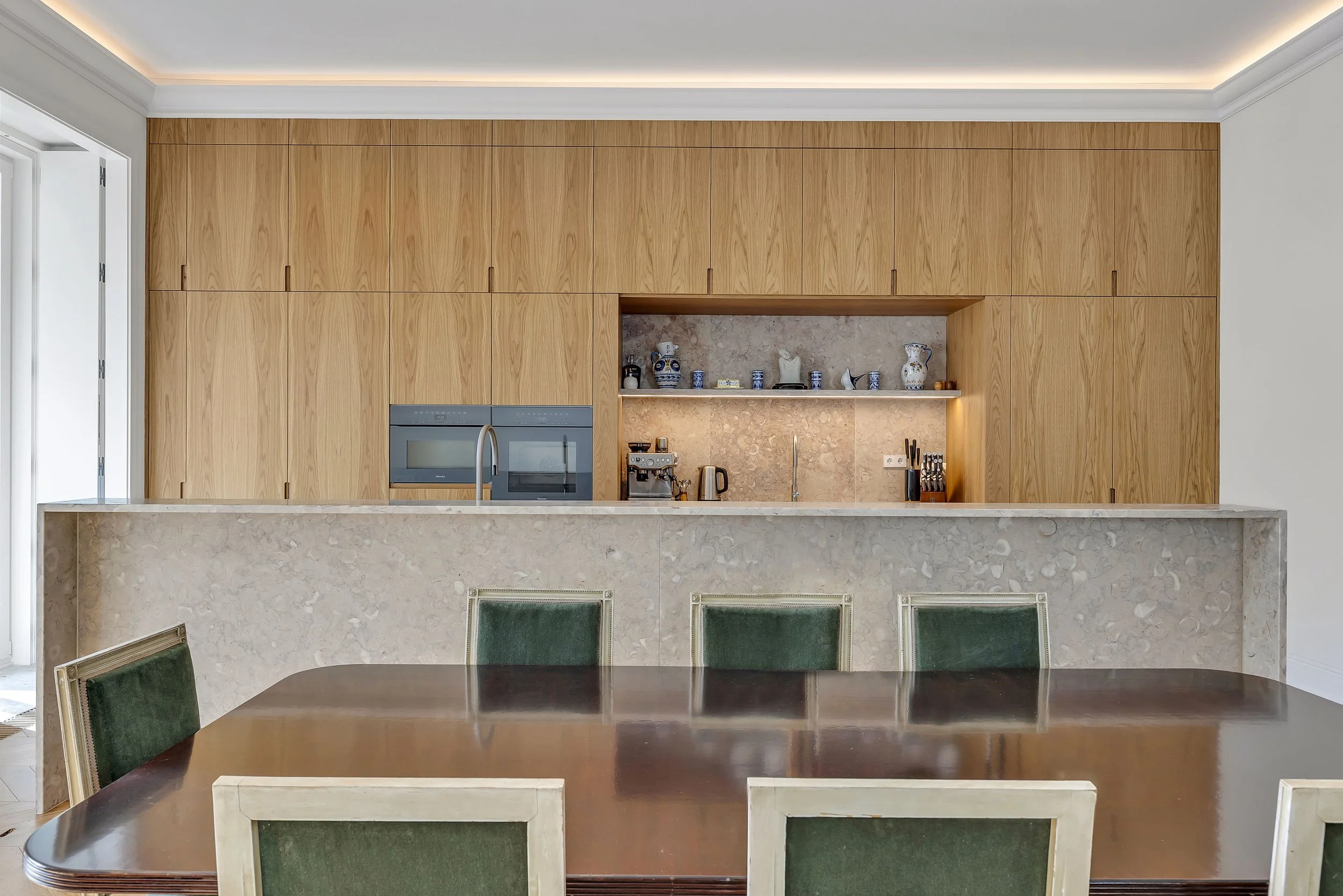 Cozinha moderna com armários de madeira, bancada de granito e uma mesa de jantar de madeira com cadeiras verdes