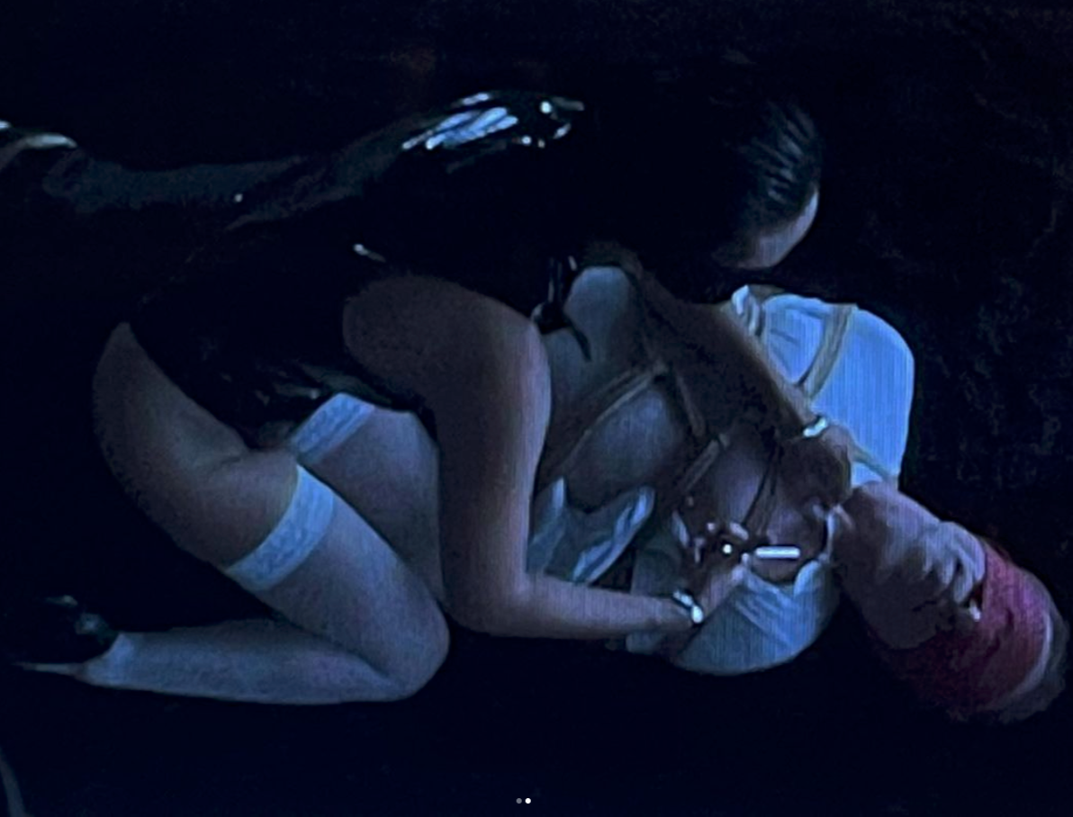 a person in a black shirt, khaki shorts, and white knee-high socks practicing rock climbing on an indoor climbing wall with harness and safety ropes