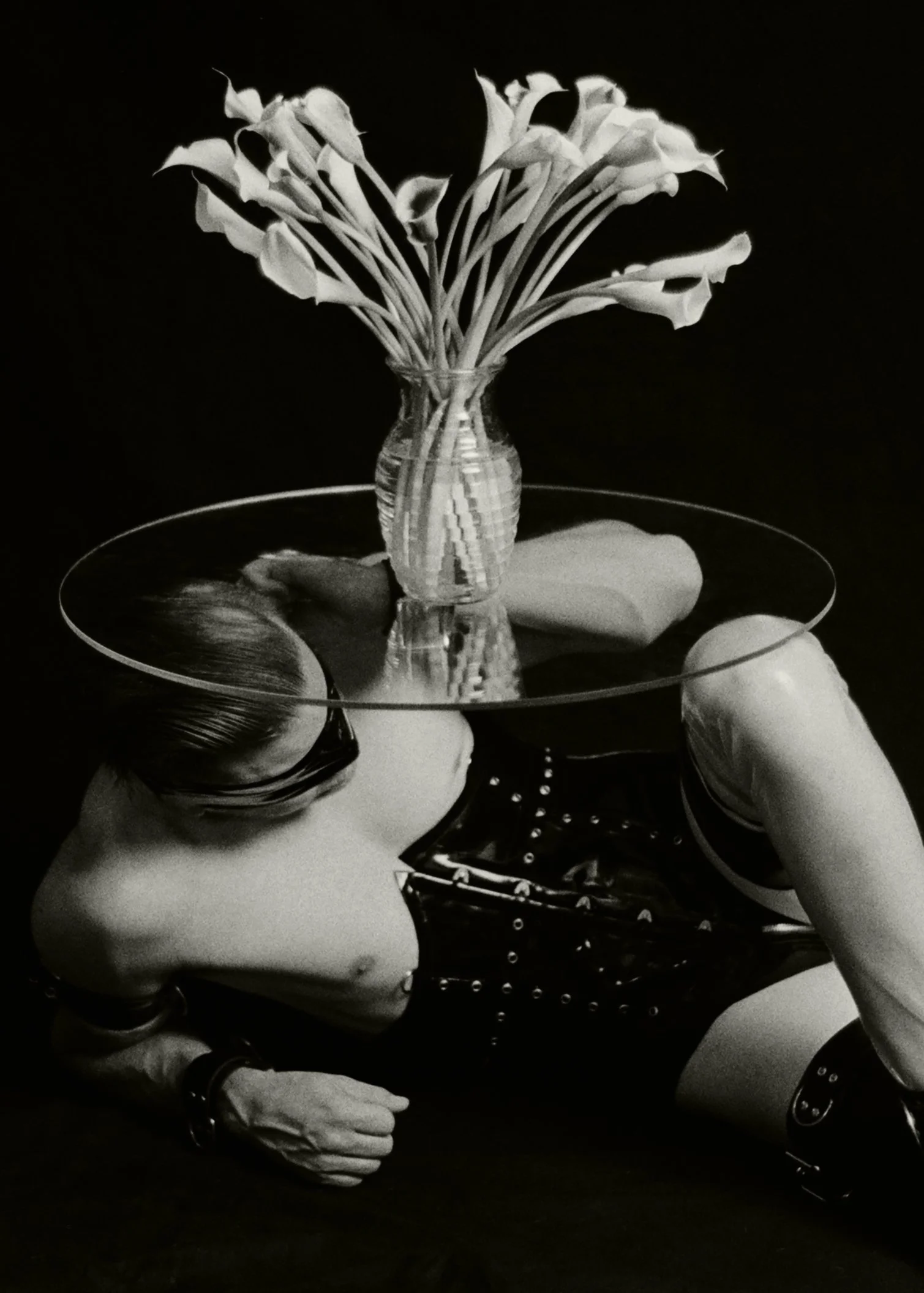 The air is still and silent, save for the soft creak of latex as he shifts beneath the glass. My male submissive—My beautiful, devoted creation—lies perfectly arranged under the cool, clear tabletop. He has become the very foundation, a living sculpt