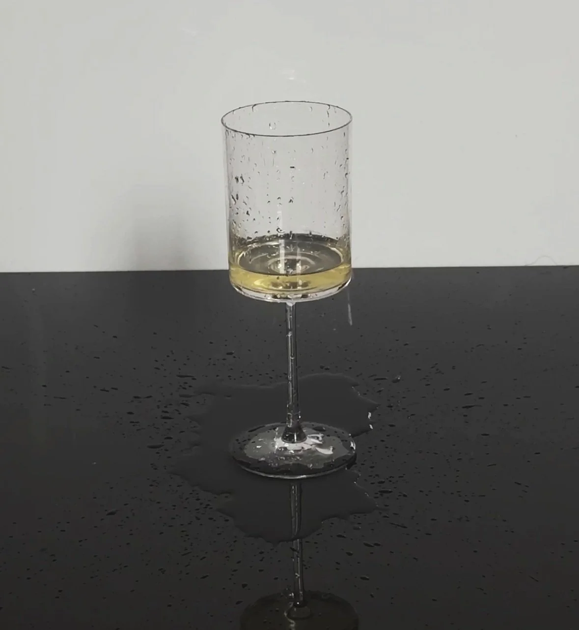 Wine glass with liquid on a wet, reflective surface.