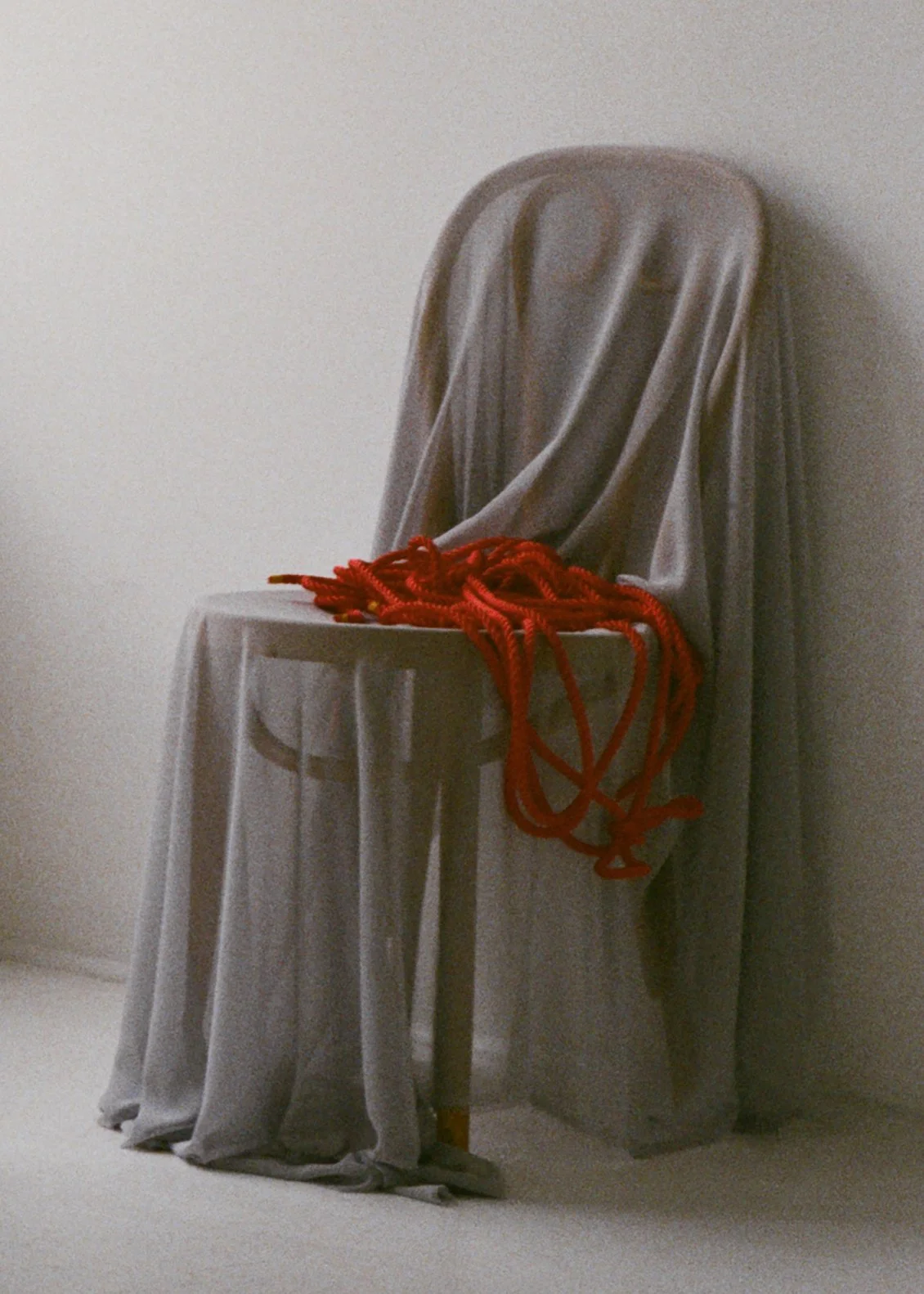 A wooden chair draped with a gray cloth and a pile of red rope placed on the seat.