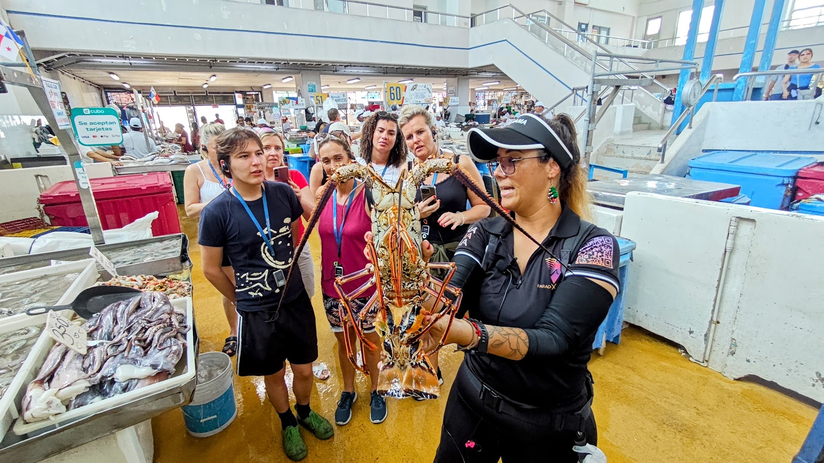 Woman holding a large spiny lobster as travelers watch during the Markets Adventure tour at Panama City’s seafood market.