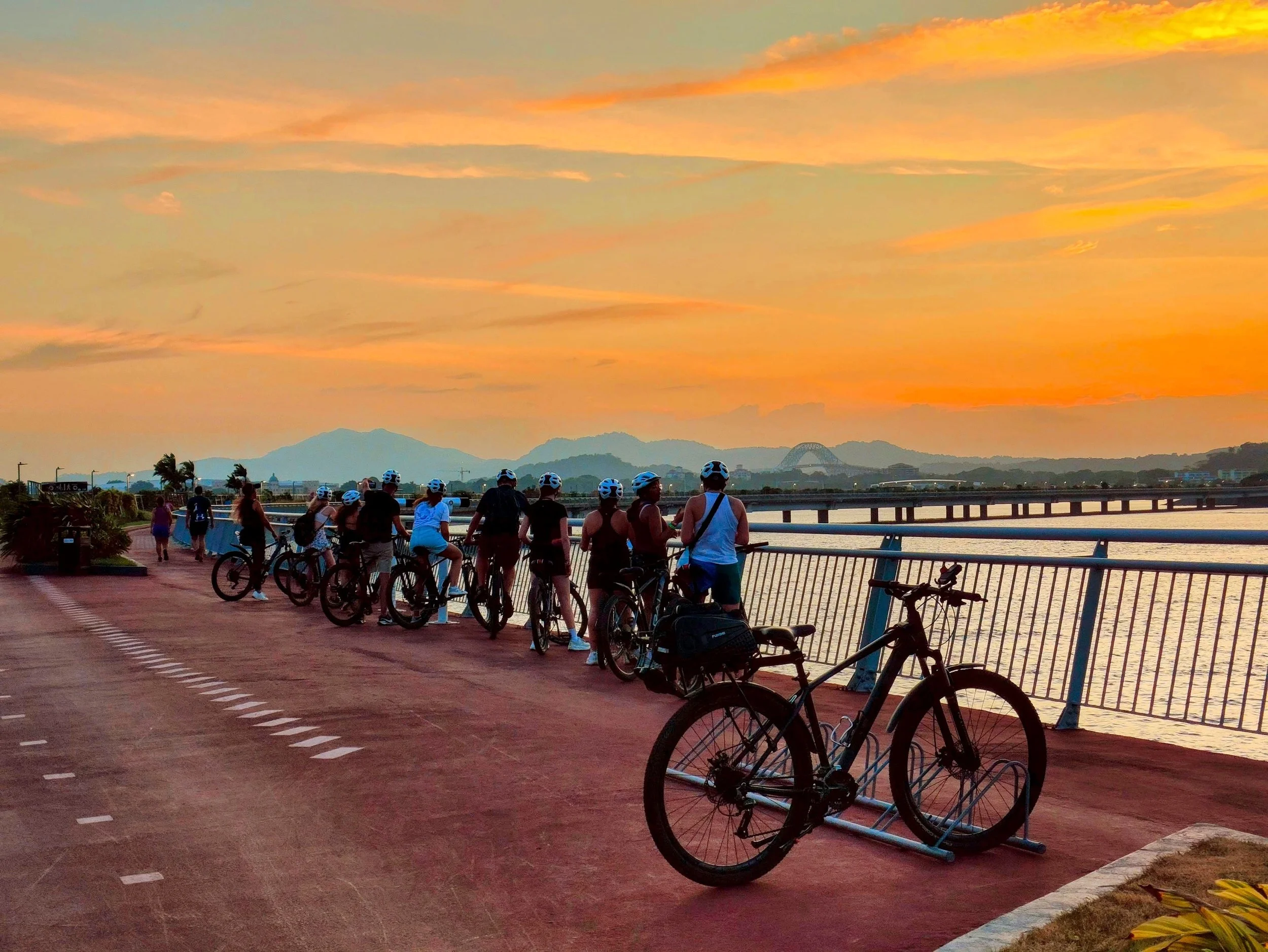 Cyclists gathered along Cinta Costera during an orange sunset on the Sunset Bike Tour in Panama City.