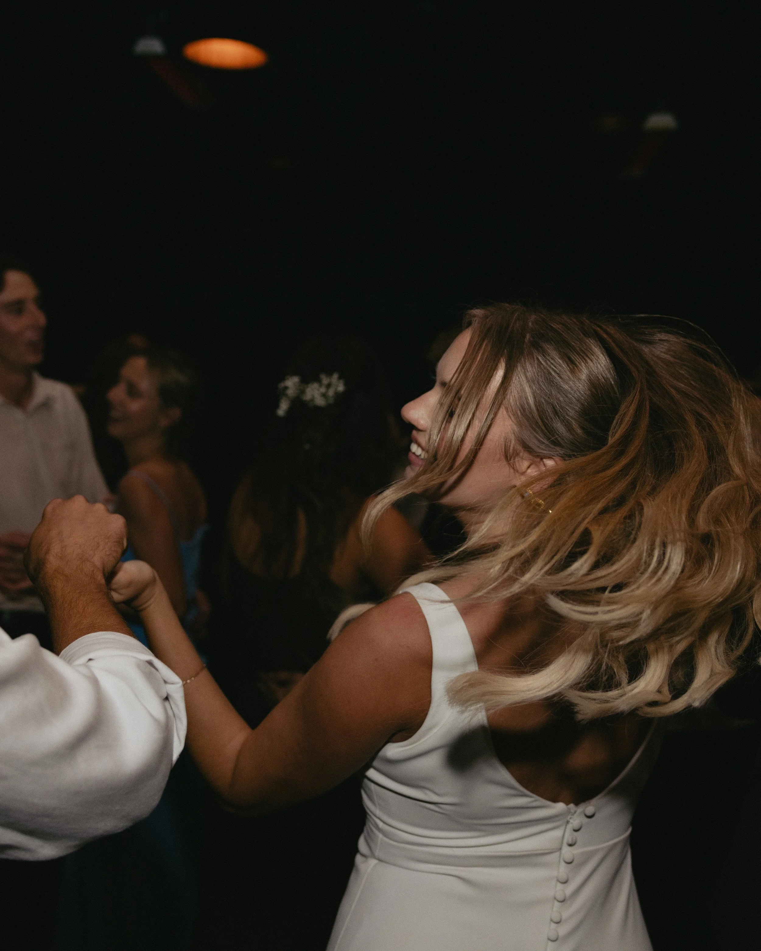 A woman in a white dress dancing and smiling with a man at a social event or party, with other people in the background.