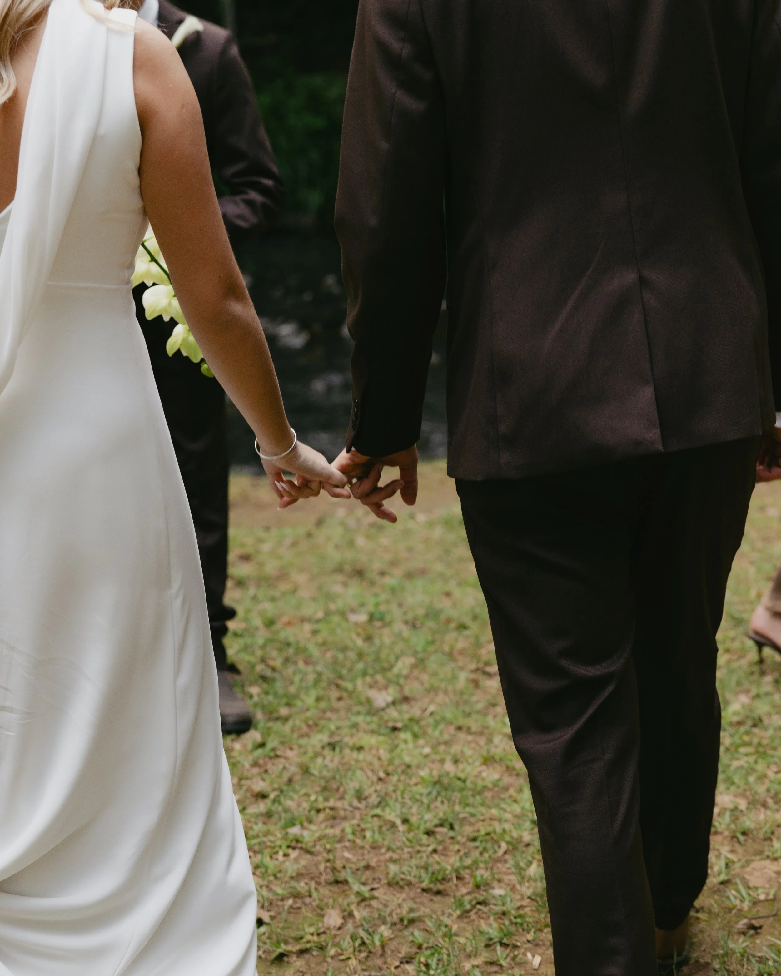 A bride and groom holding hands during their wedding ceremony outdoors.