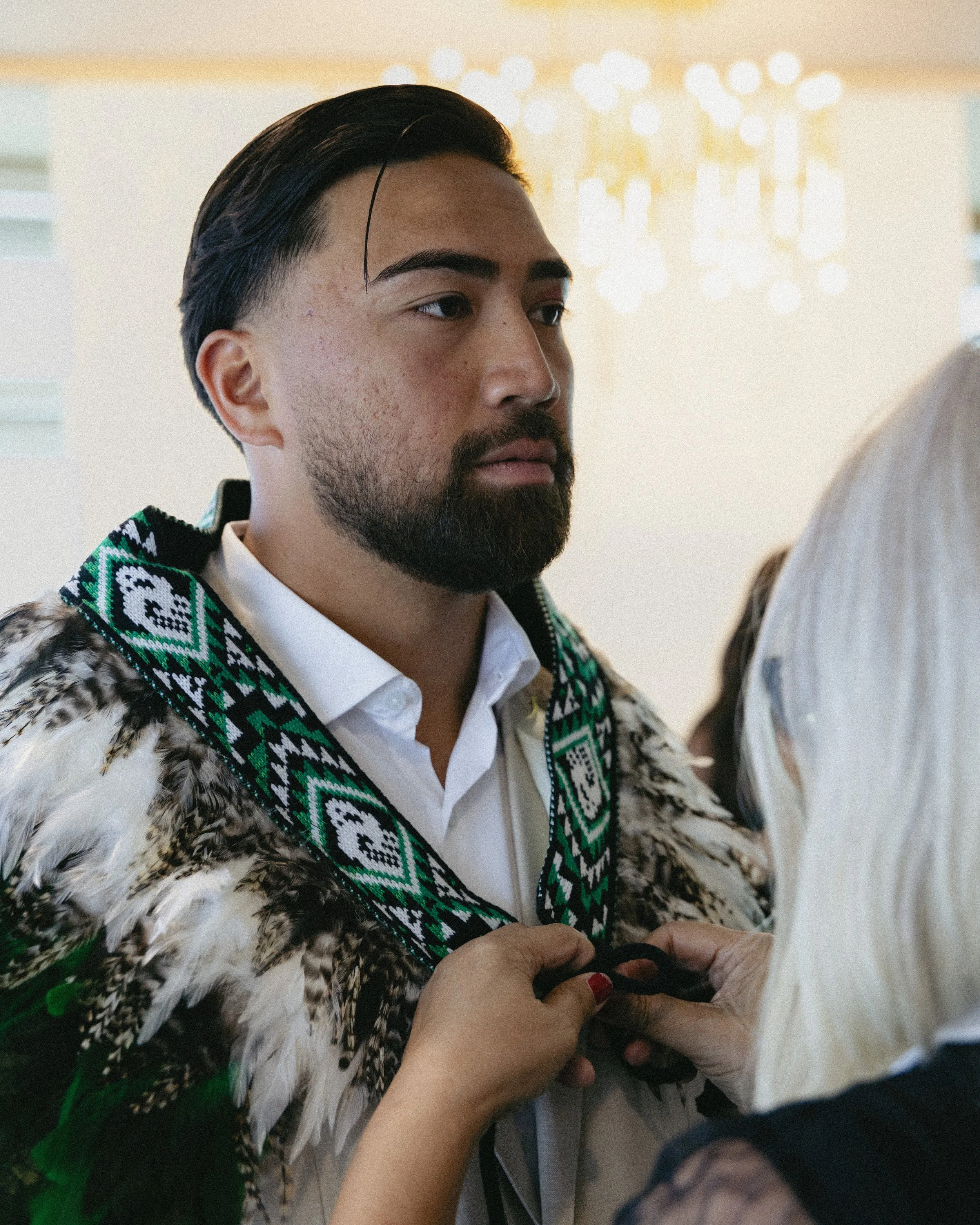 Person with traditional Indigenous attire being adorned with a necklace during a ceremony or gathering.