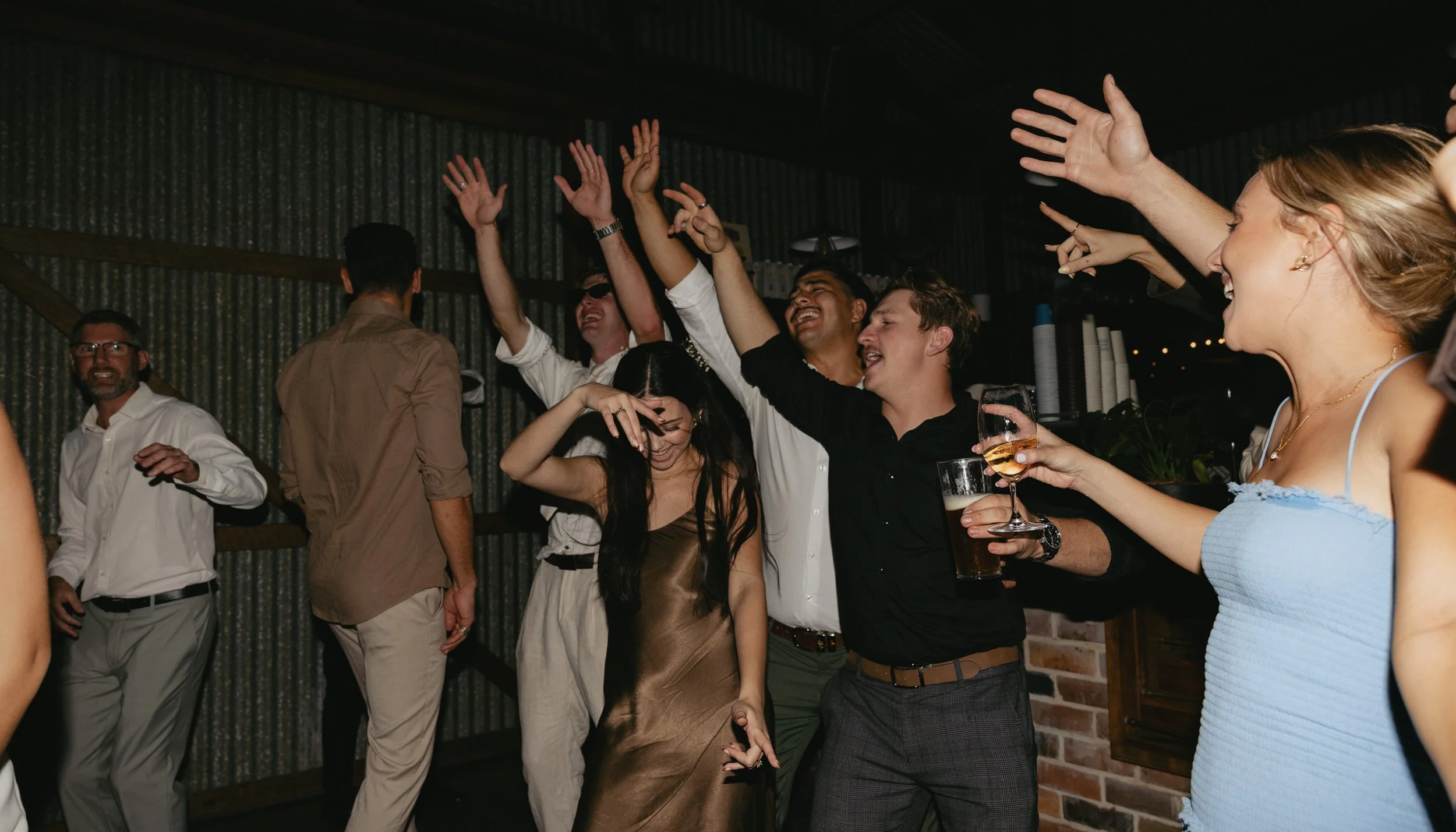 Group of people dancing and celebrating at a party or social gathering indoors, smiling and raising their hands.