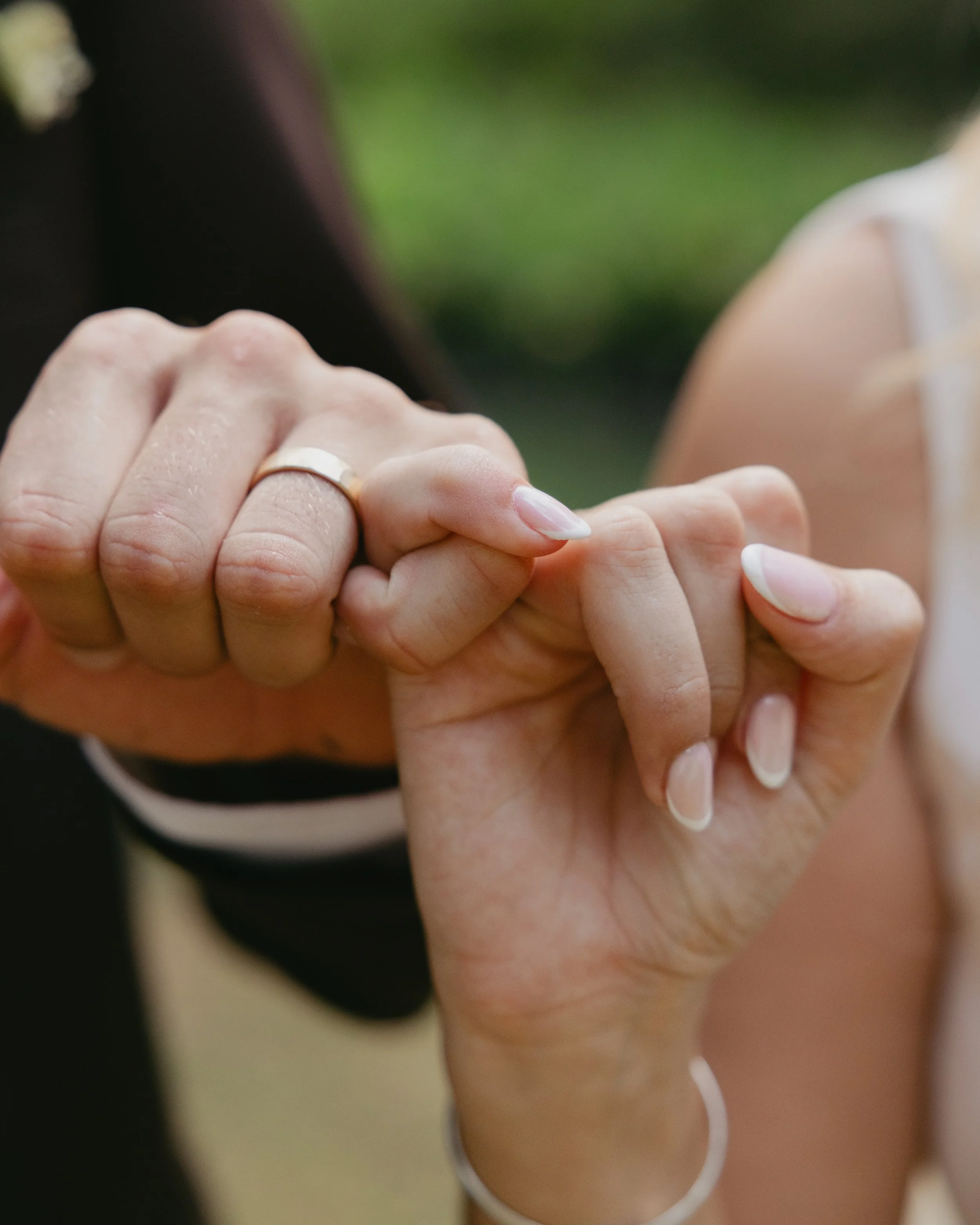 Close-up of a man and woman holding hands, with the man wearing a wedding ring on his left hand, and their fingers intertwined.