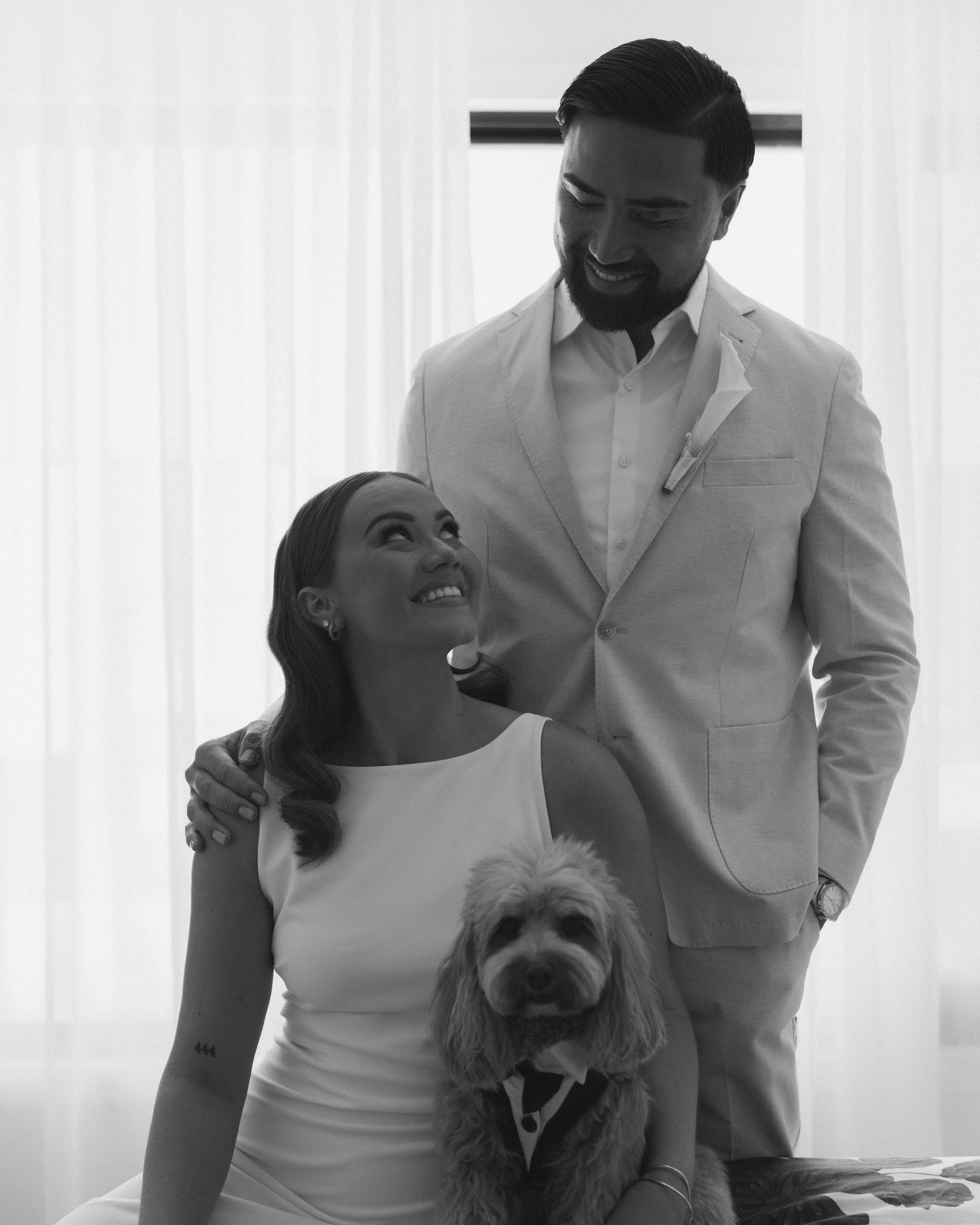 A couple, a woman and a man, with a dog, smiling at each other, in a professional setting, in black and white.