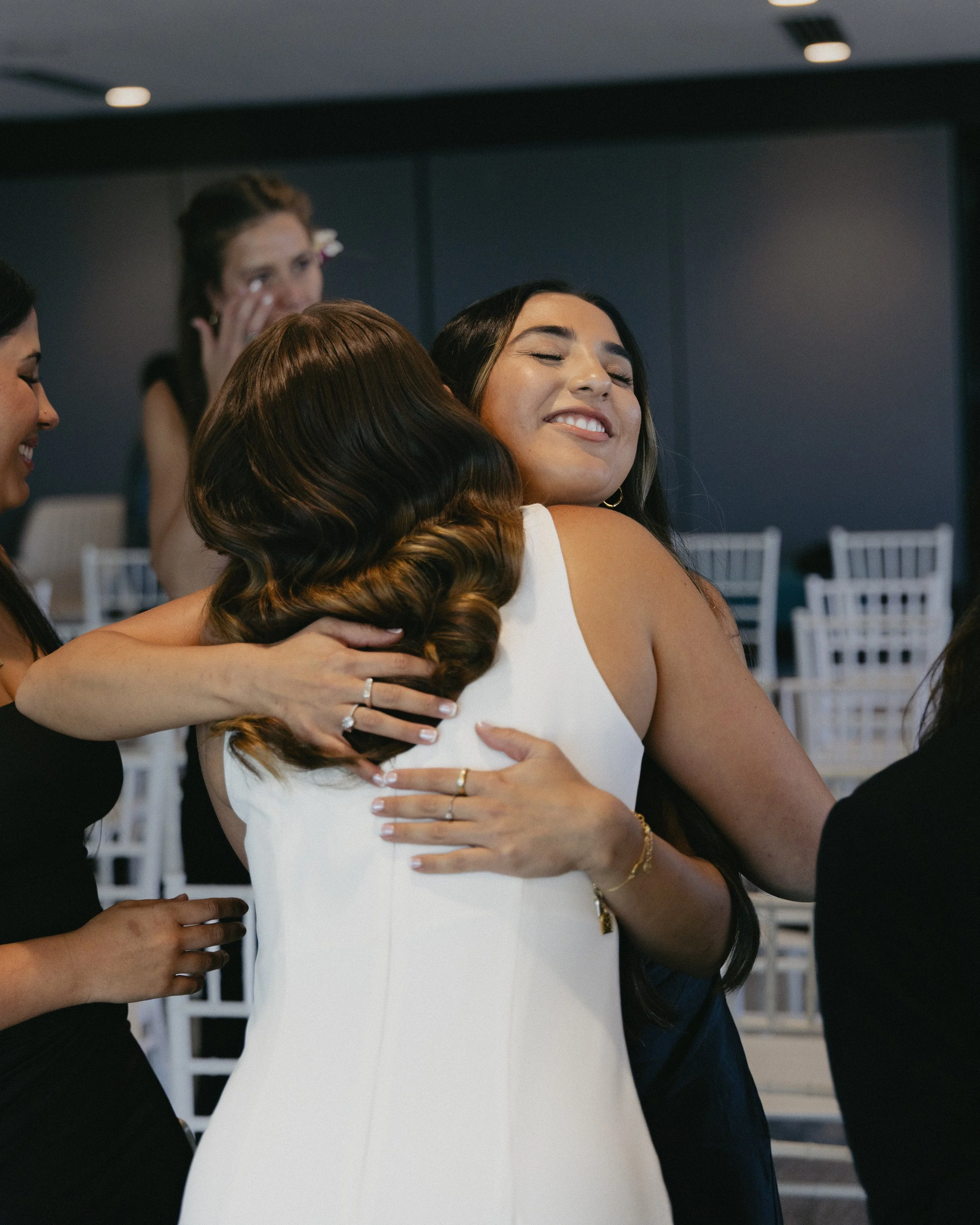 Two women hugging each other with happy expressions at a social gathering.
