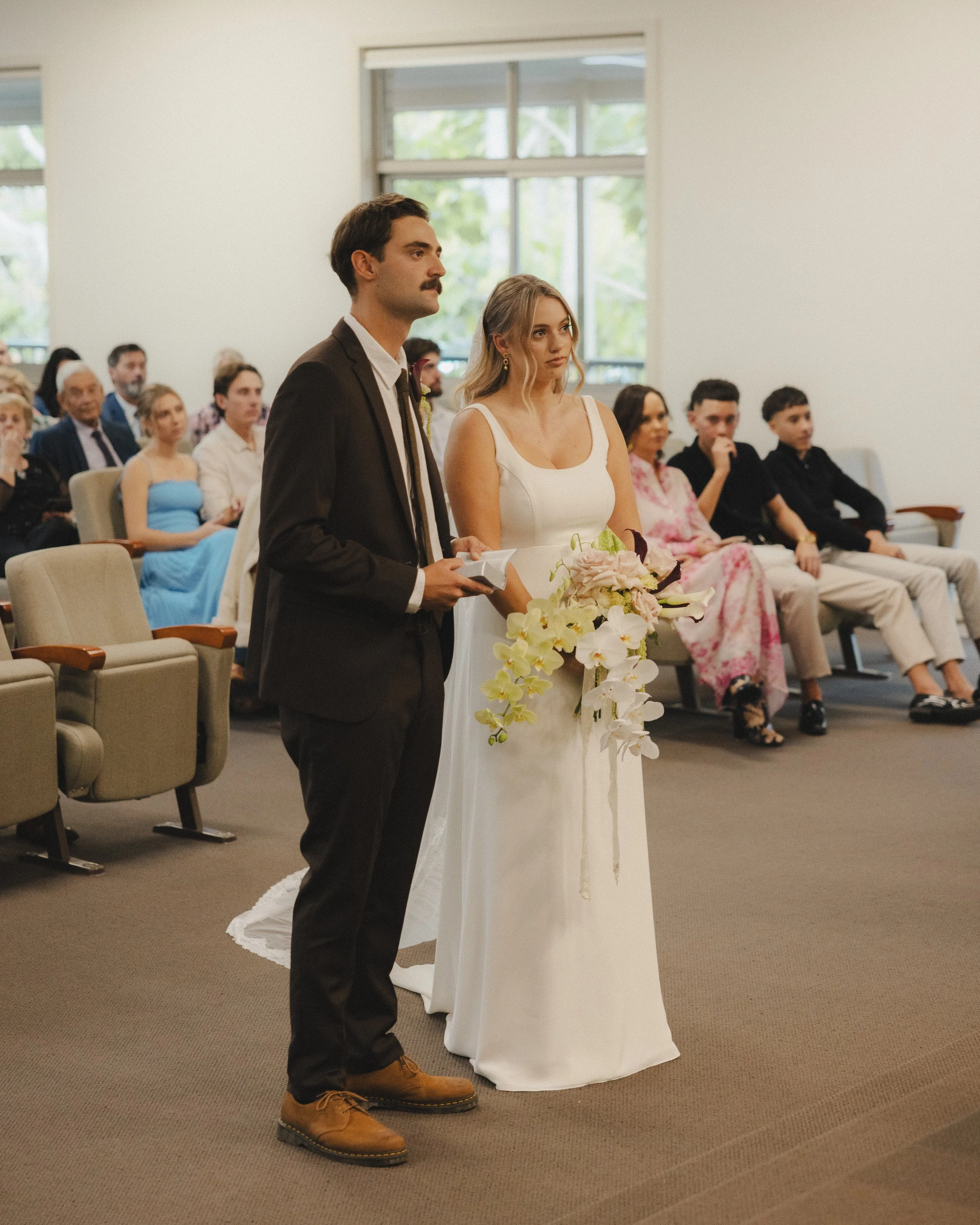 A couple getting married stands at the altar during a wedding ceremony, with guests sitting in the background.