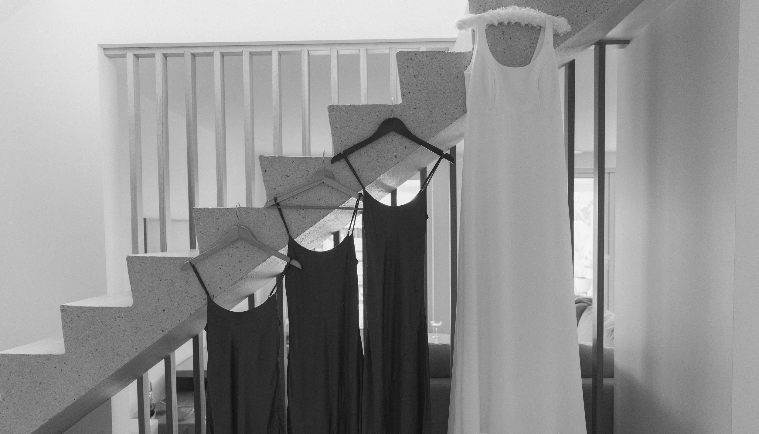 White wedding dress hanging next to black dresses on a staircase railing.