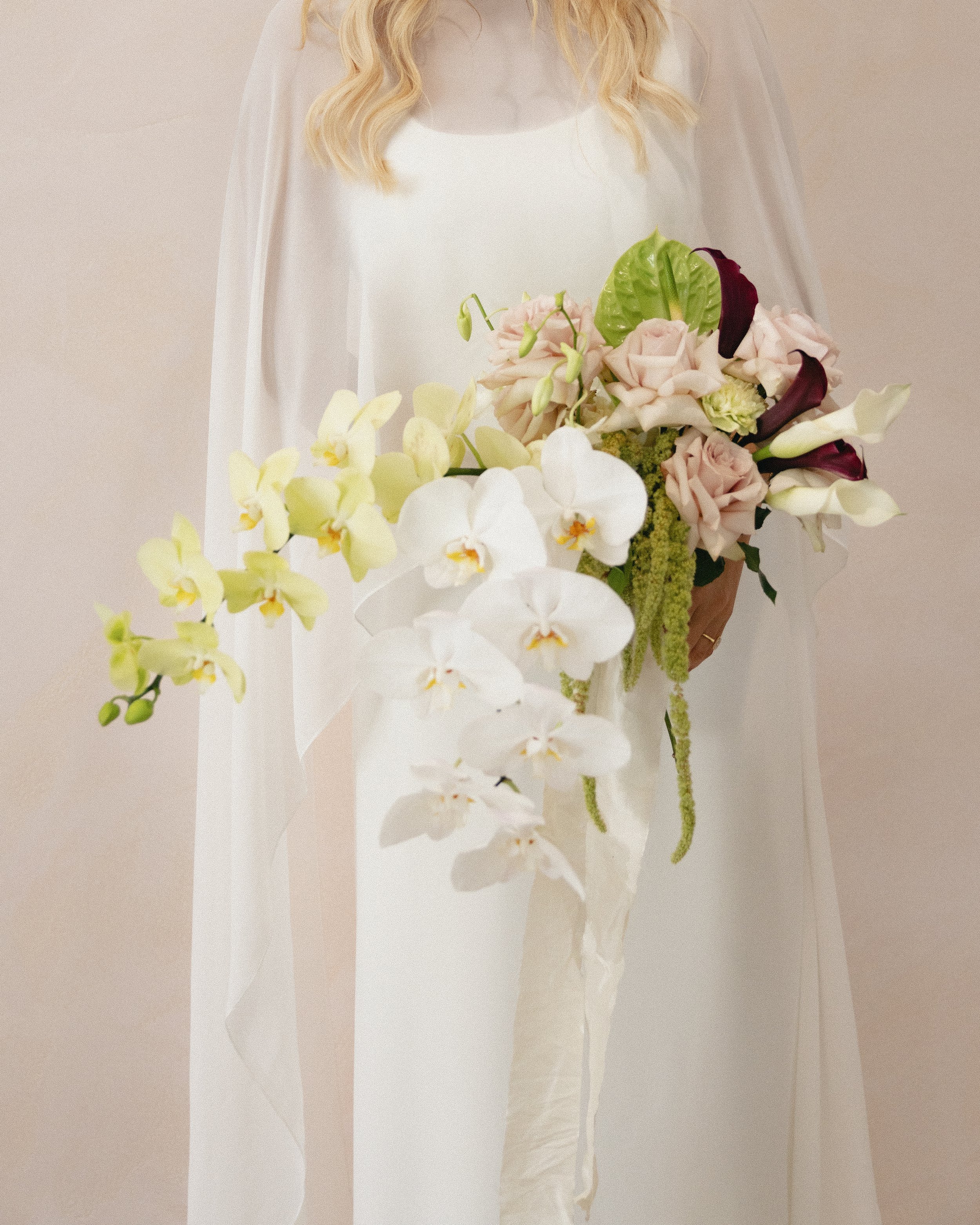 Person in a white dress holding a large bouquet of white, pink, and dark red flowers