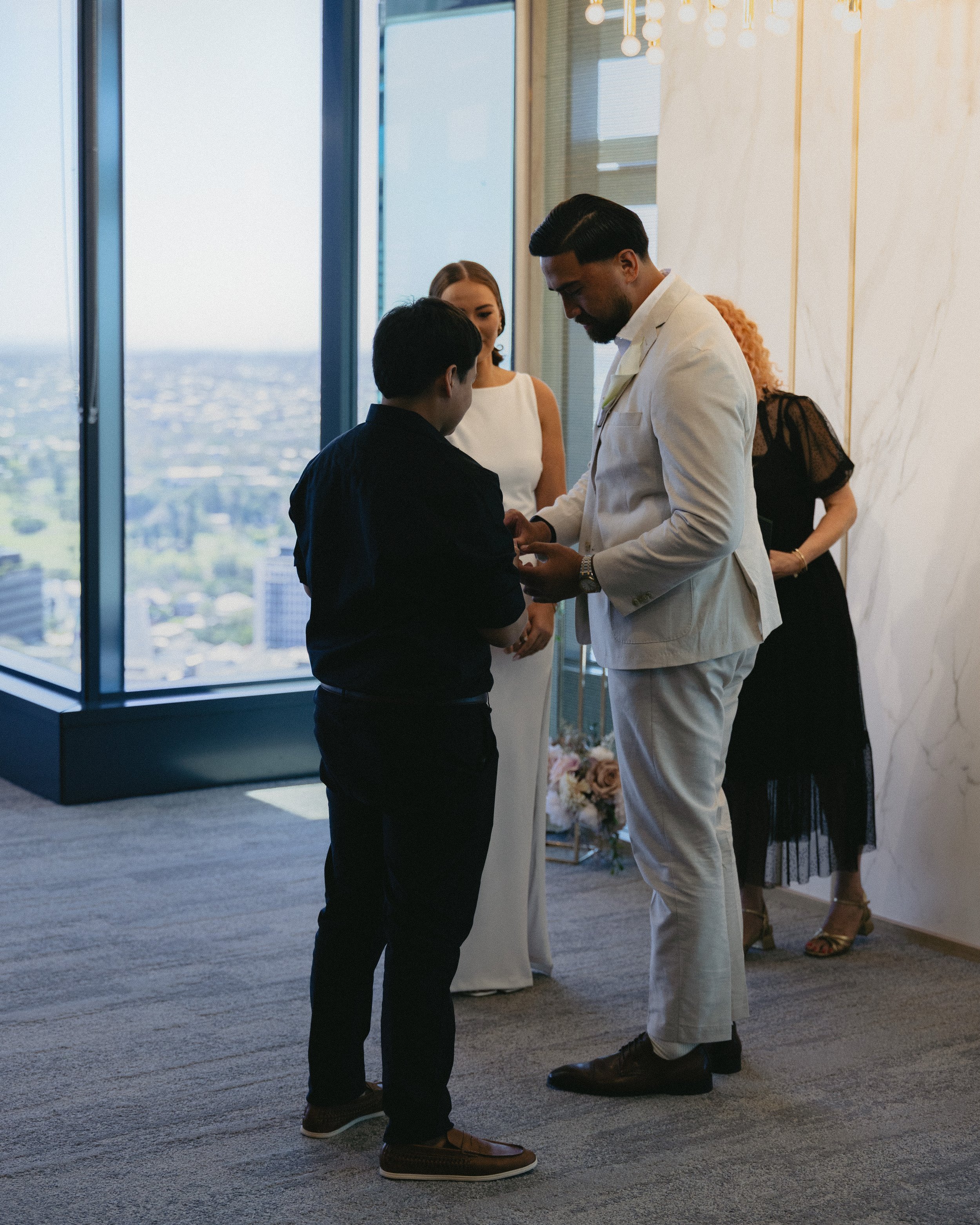 A wedding ceremony with a man and woman exchanging vows in front of a officiant and witnesses in a tall cityscape building.