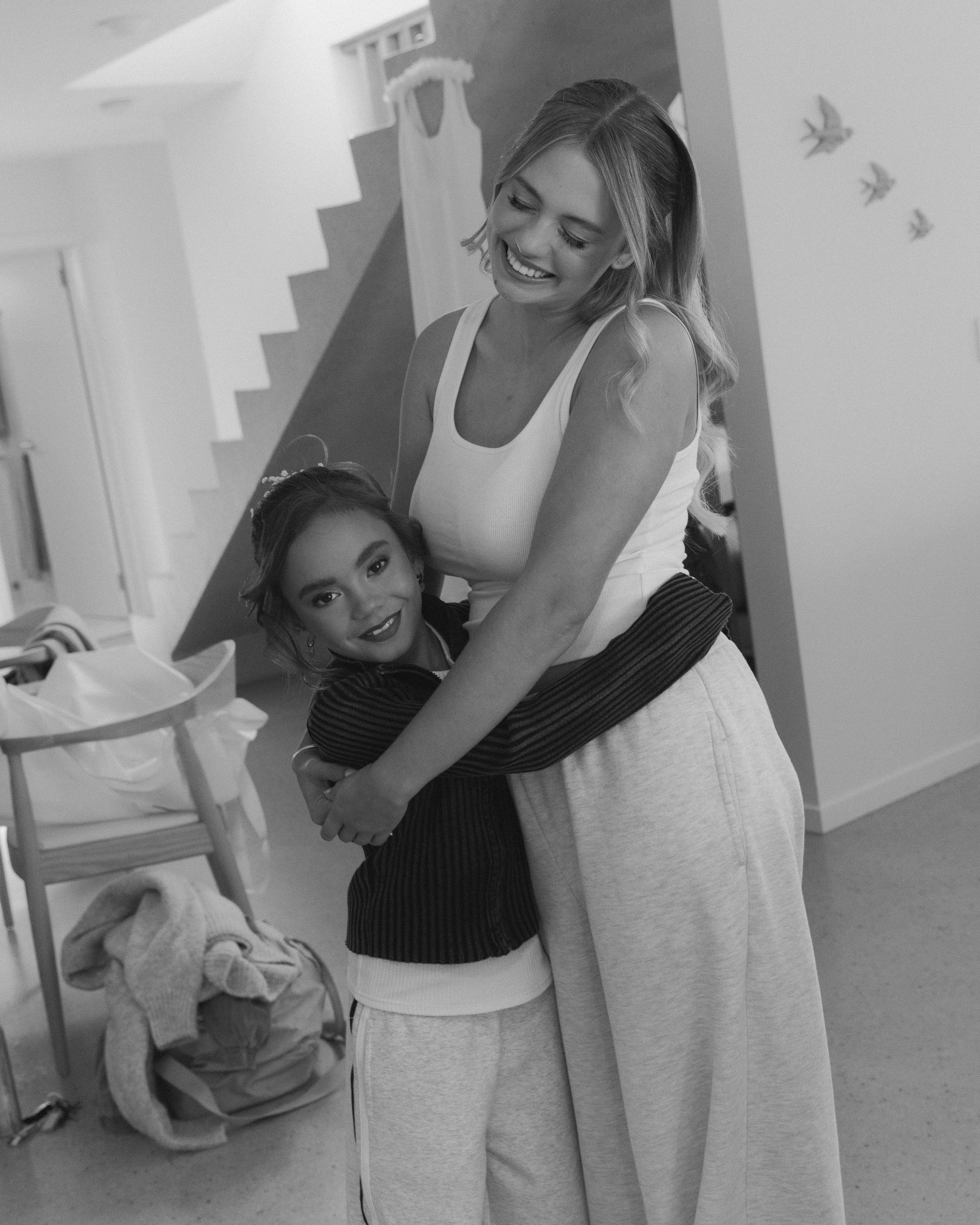 A smiling woman hugging a young girl in a home setting.