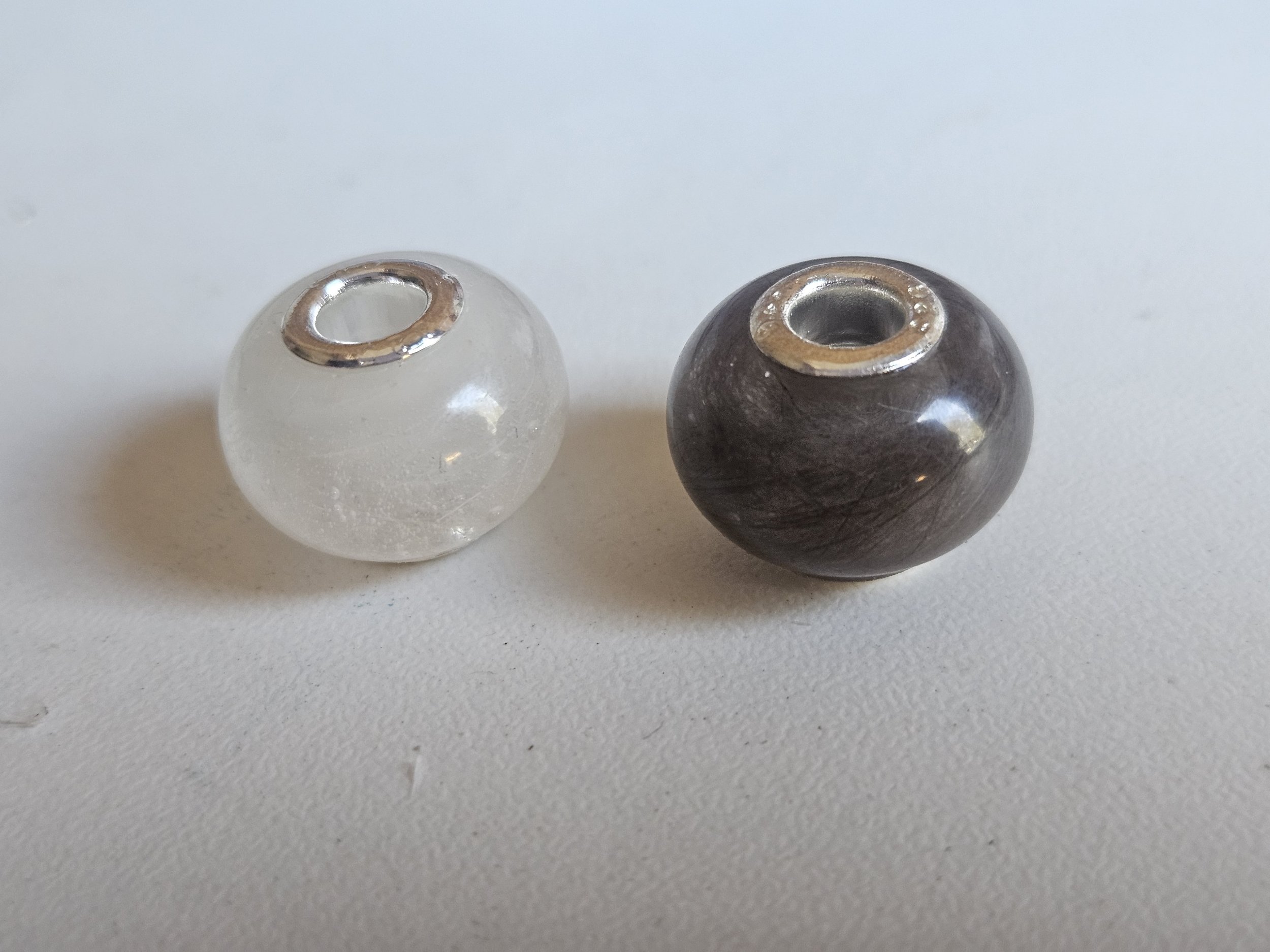 2 pandora-style beads filled with beloved pet fur. One white bunny fluff. one grey kitten fluff. featuring sterling silver cores. 