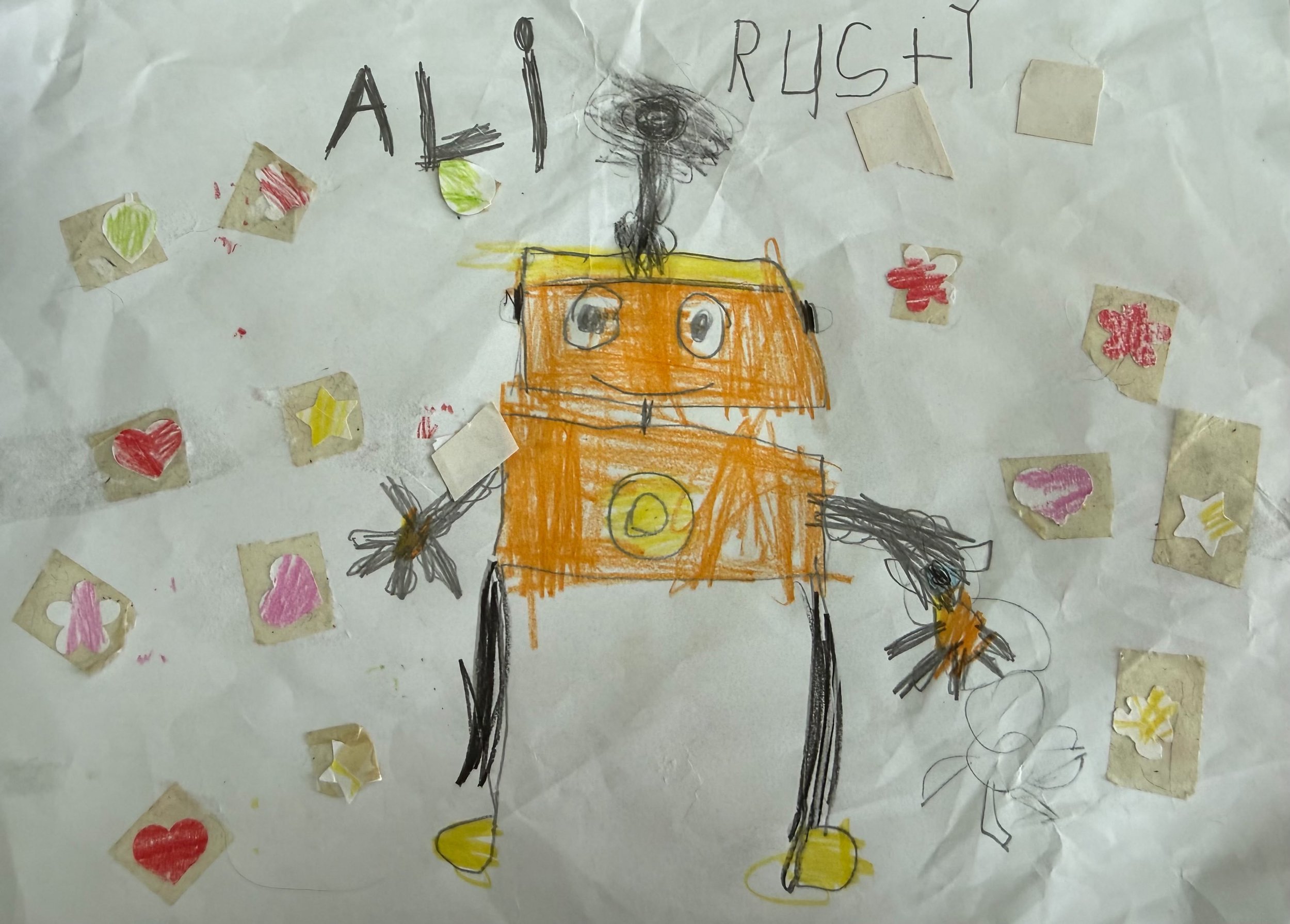 Child's drawing of a robot with a rectangular orange body, round eyes, yellow feet, gray arms, and a black scribbled smoke or steam coming out of its head; surrounded by cut-out heart, star, and flower shapes.