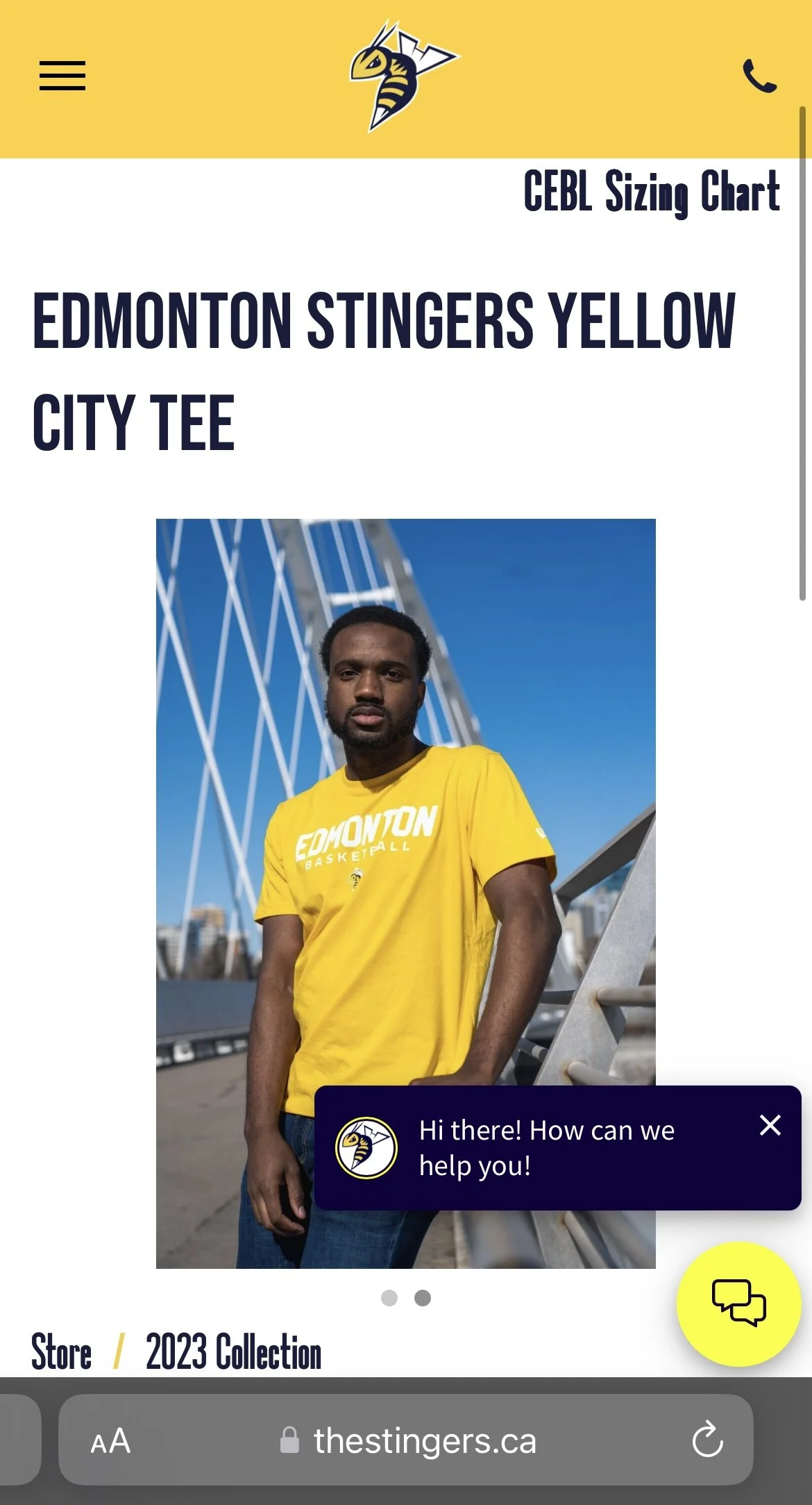A man wearing a yellow Edmonton Stingers basketball T-shirt stands outdoors against a blue sky with modern bridge architecture in the background. There is a chat icon and a message bubble at the bottom right corner of the image.