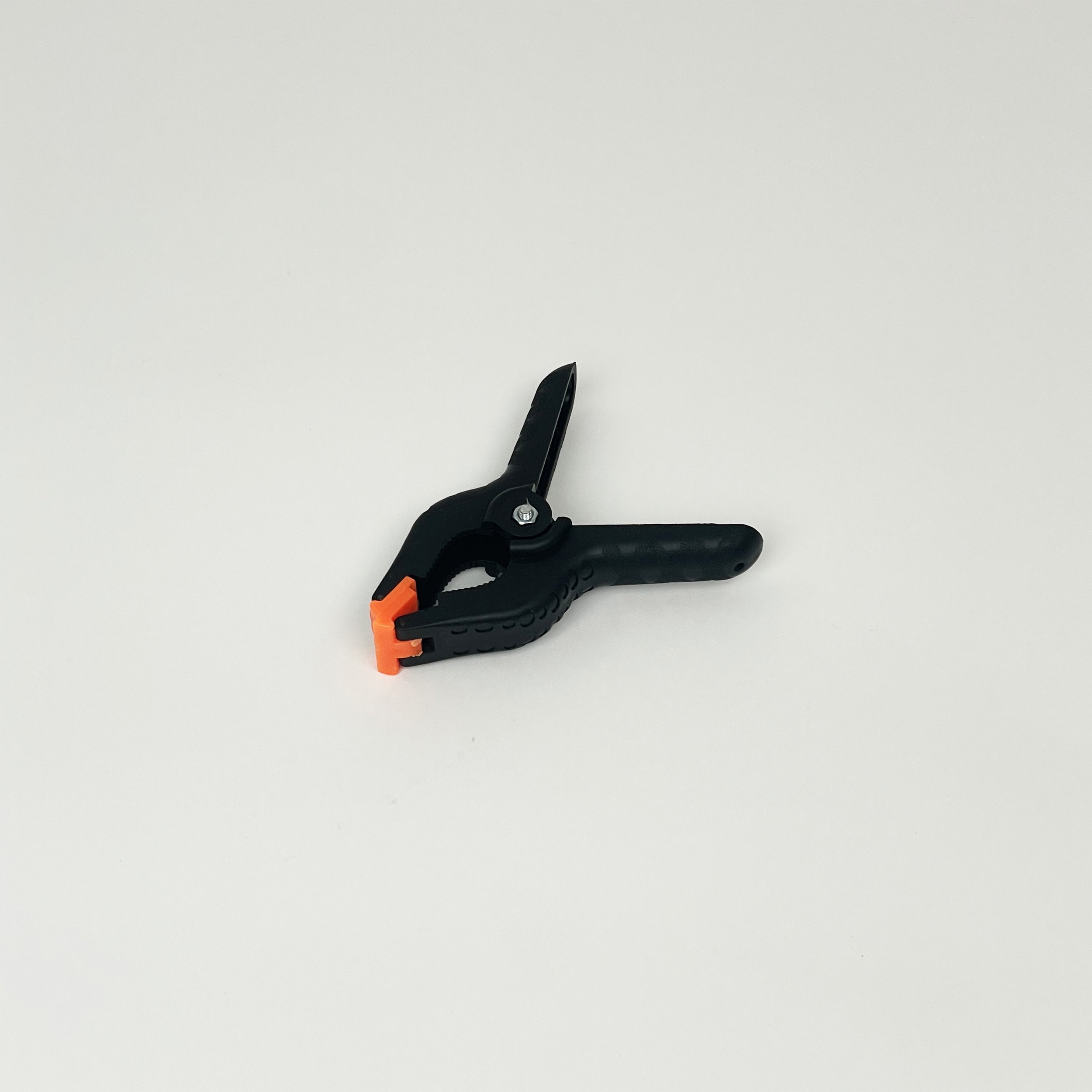 Plastic spring clamp with black handles and orange tips on a light background.