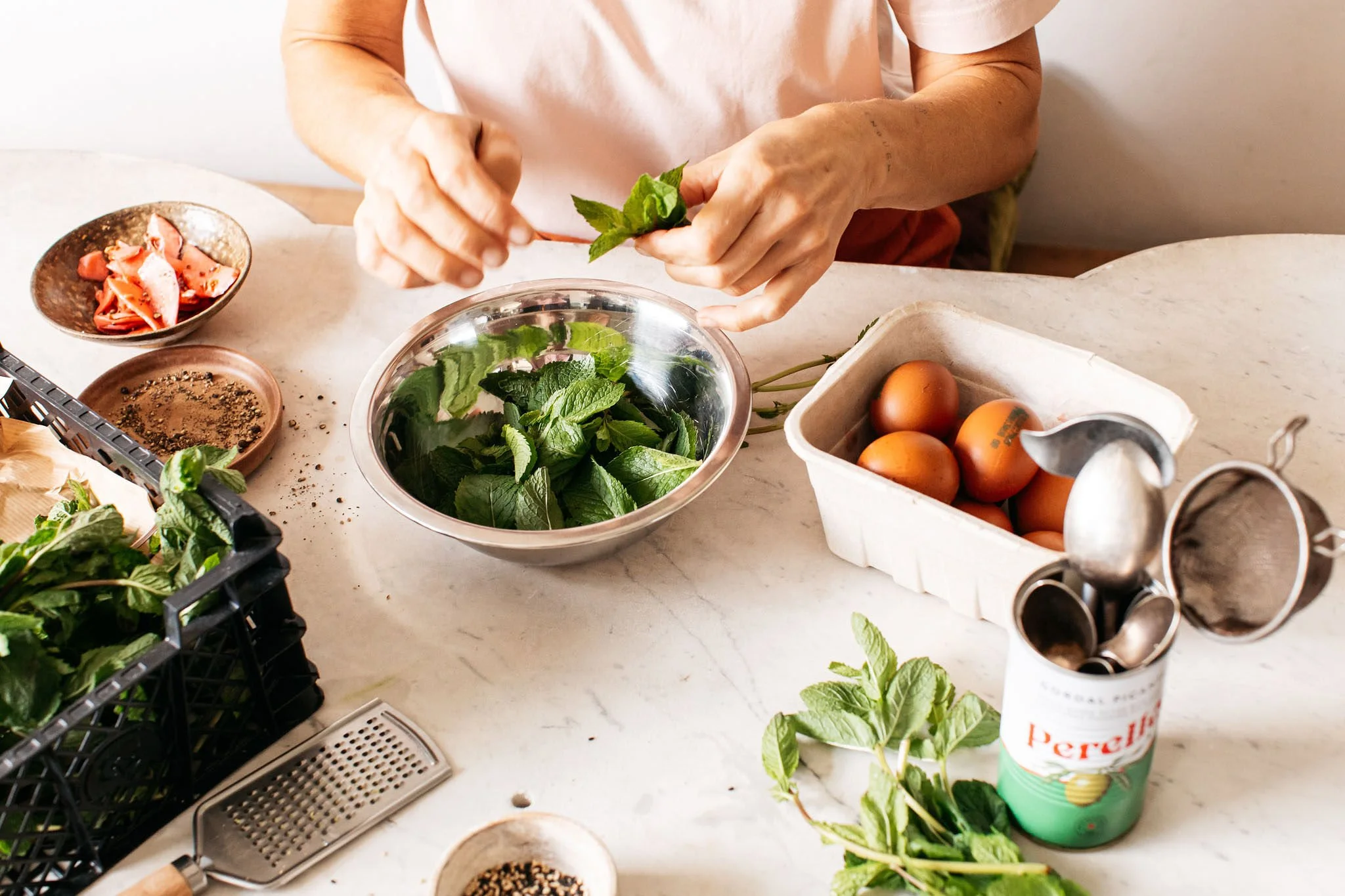 Person preparing fresh mint leaves at a kitchen counter with eggs, herbs, and spices around.