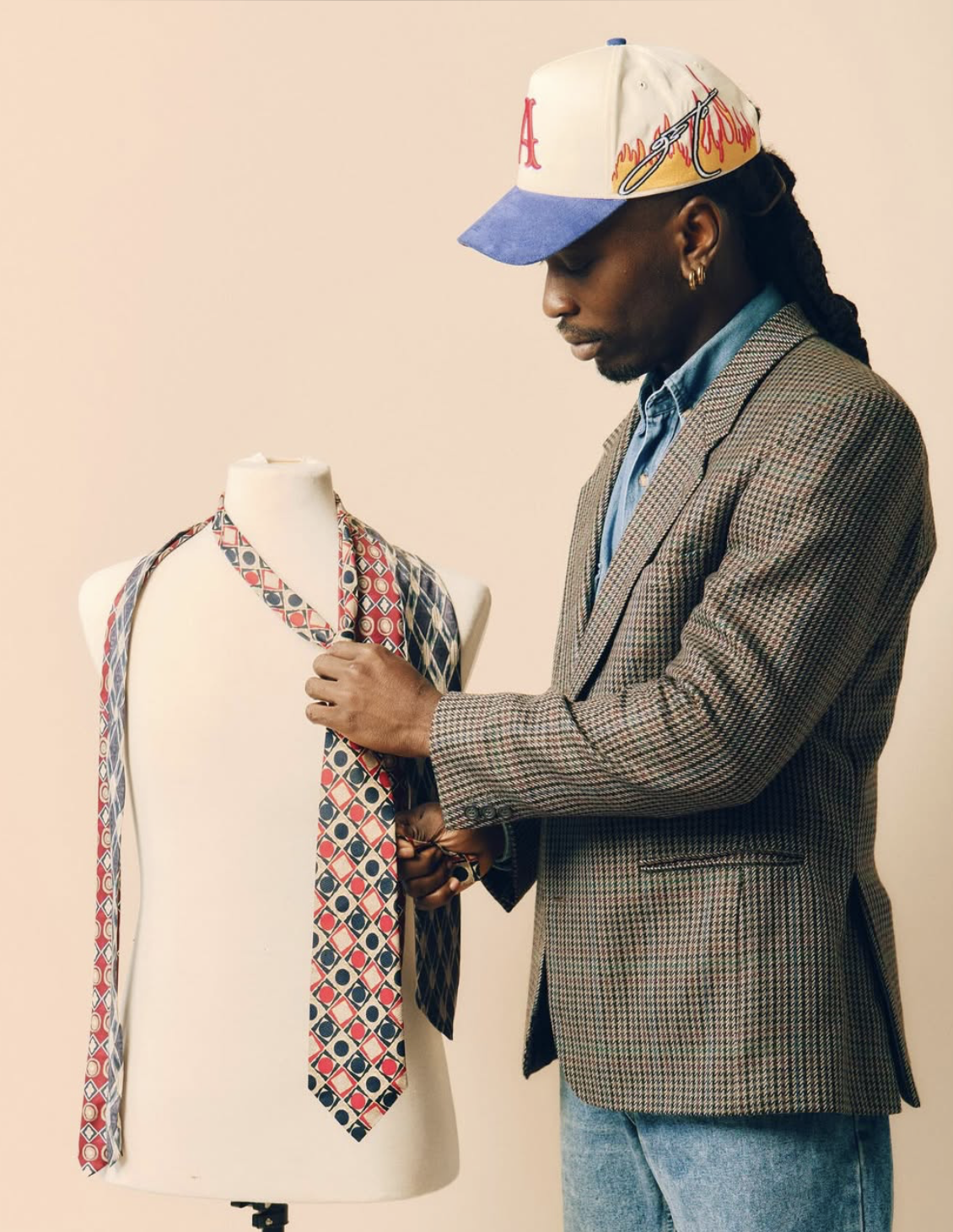 Man in a checkered blazer and a blue shirt adjusting a patterned scarf on a mannequin.