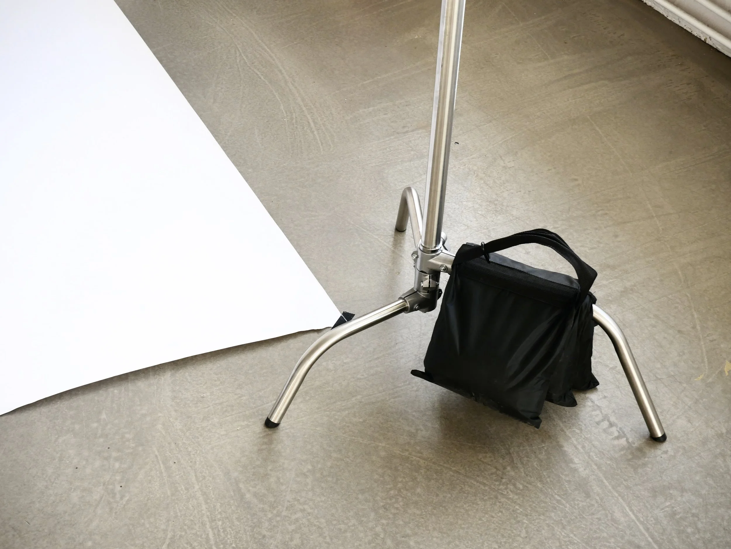 Studio photography setup with a white backdrop, a metal stand, and a black carrying bag on the floor.