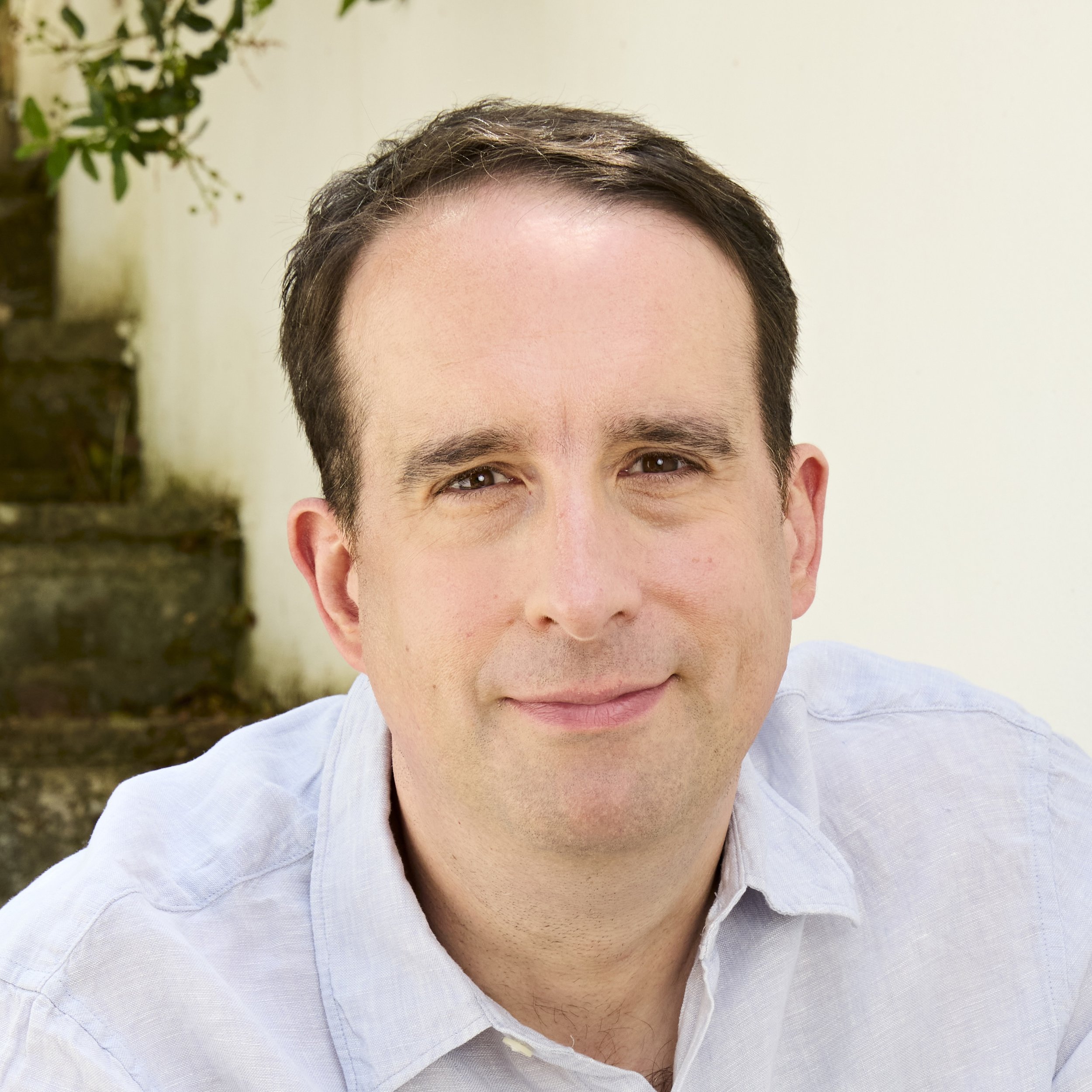 Author Jack Jewers half-smiles at the camera. He is in his 40s and has dark hair. He is wearing a light blue shirt.