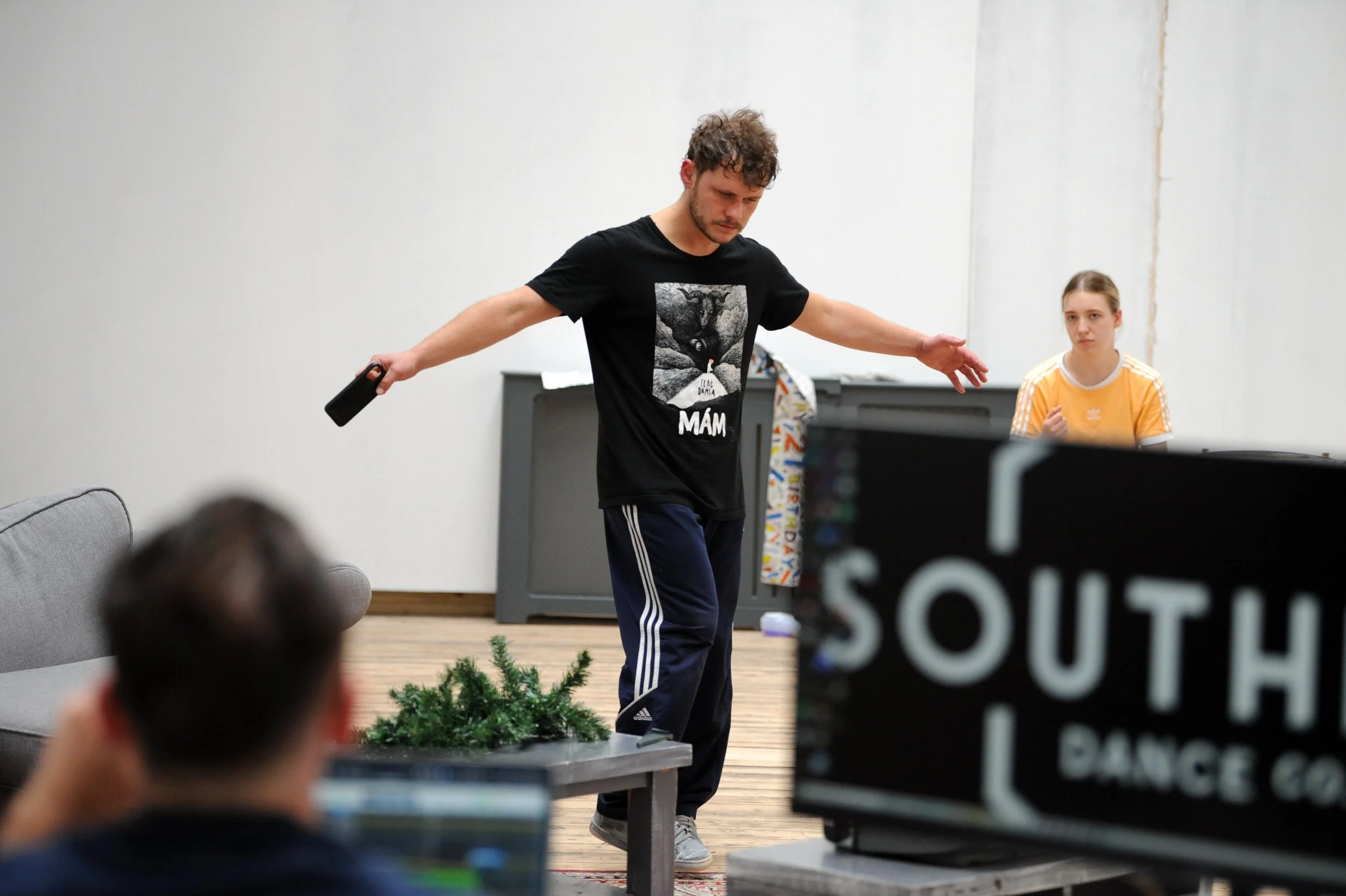 man in black tee shirt with arms outstretched is holding a remote