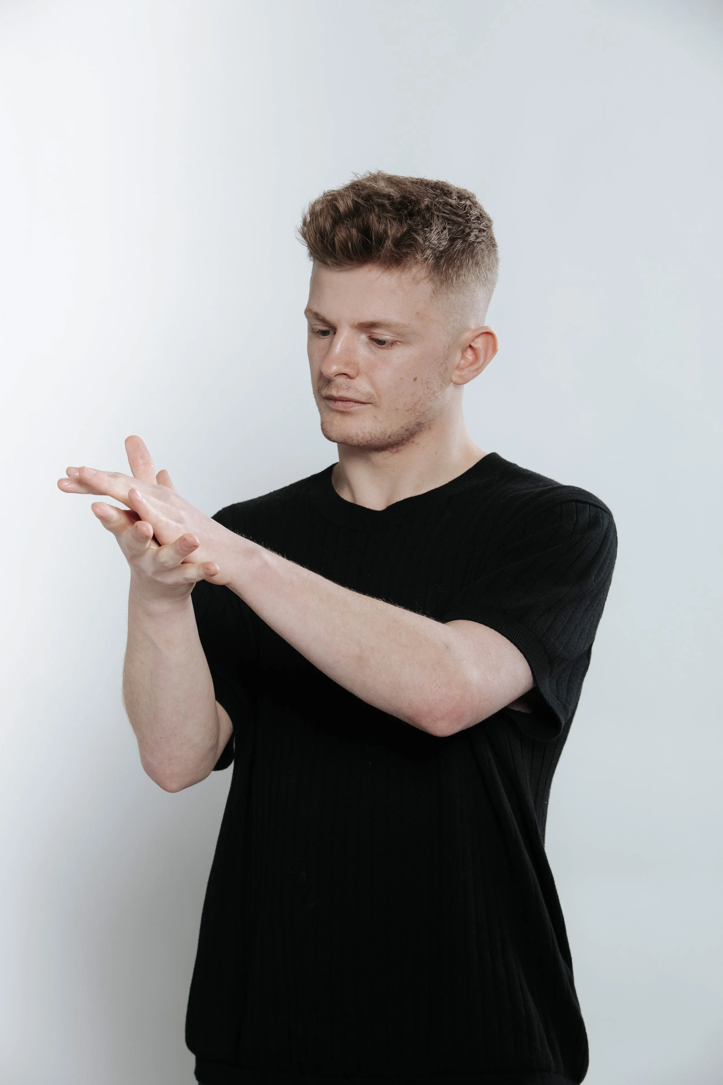 A young man with short light brown hair and blue eyes, wearing a black shirt, looking at the camera with a neutral expression against a plain light background.