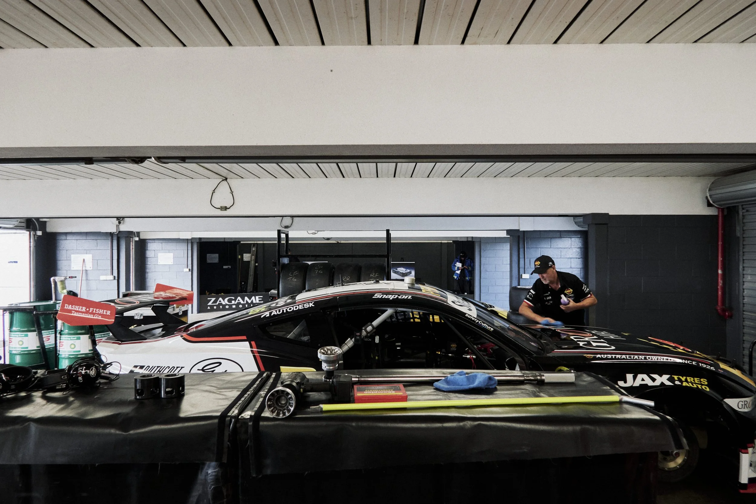 A racing car in a garage with mechanics working around it, tools and equipment in the foreground.