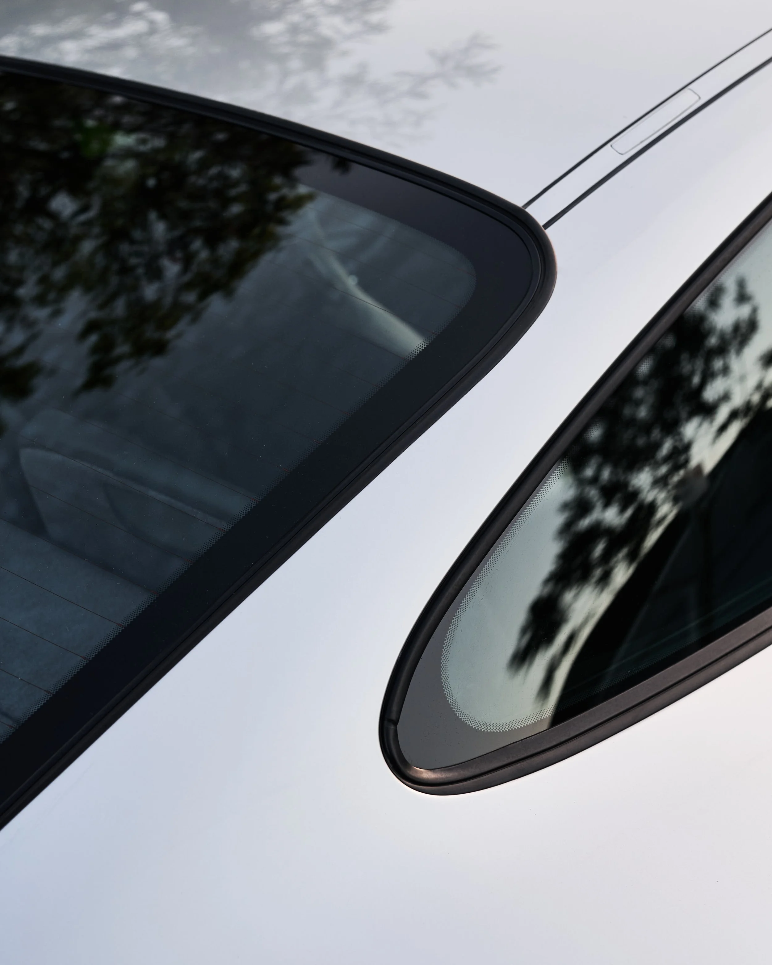 Close-up of a silver car's rear windshield and rear side window with reflections of trees.