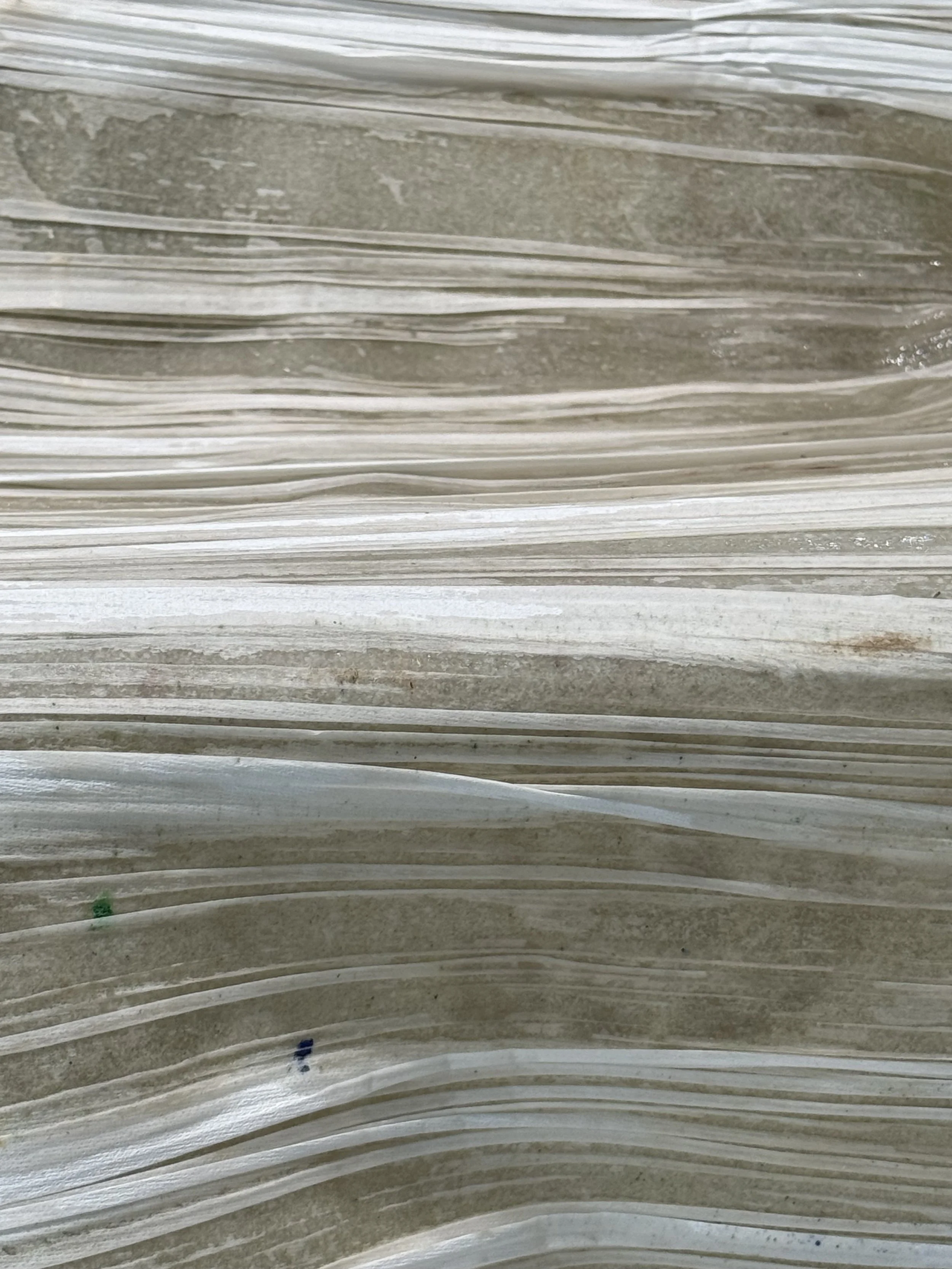 Close-up of layered, textured paper with shades of gray, white, and hints of green and blue.
